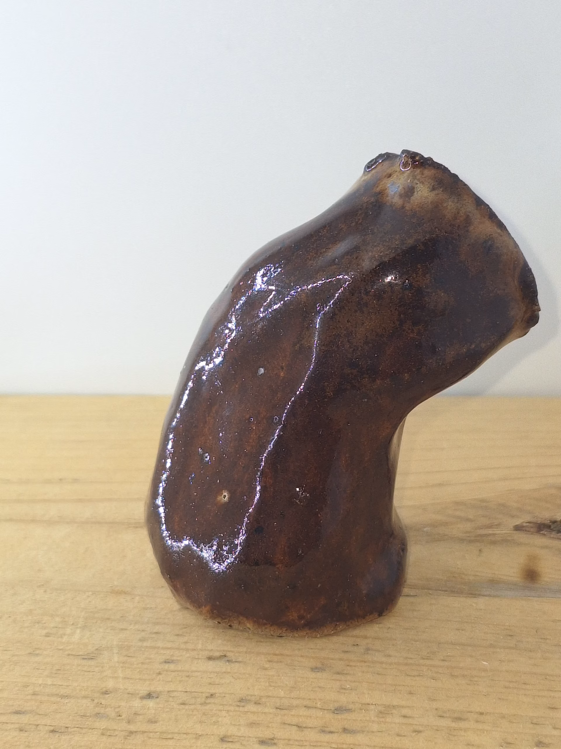 small ceramic owlet with dark brown glaze, head tilted thoughtfully, textured feather detail across face and body.