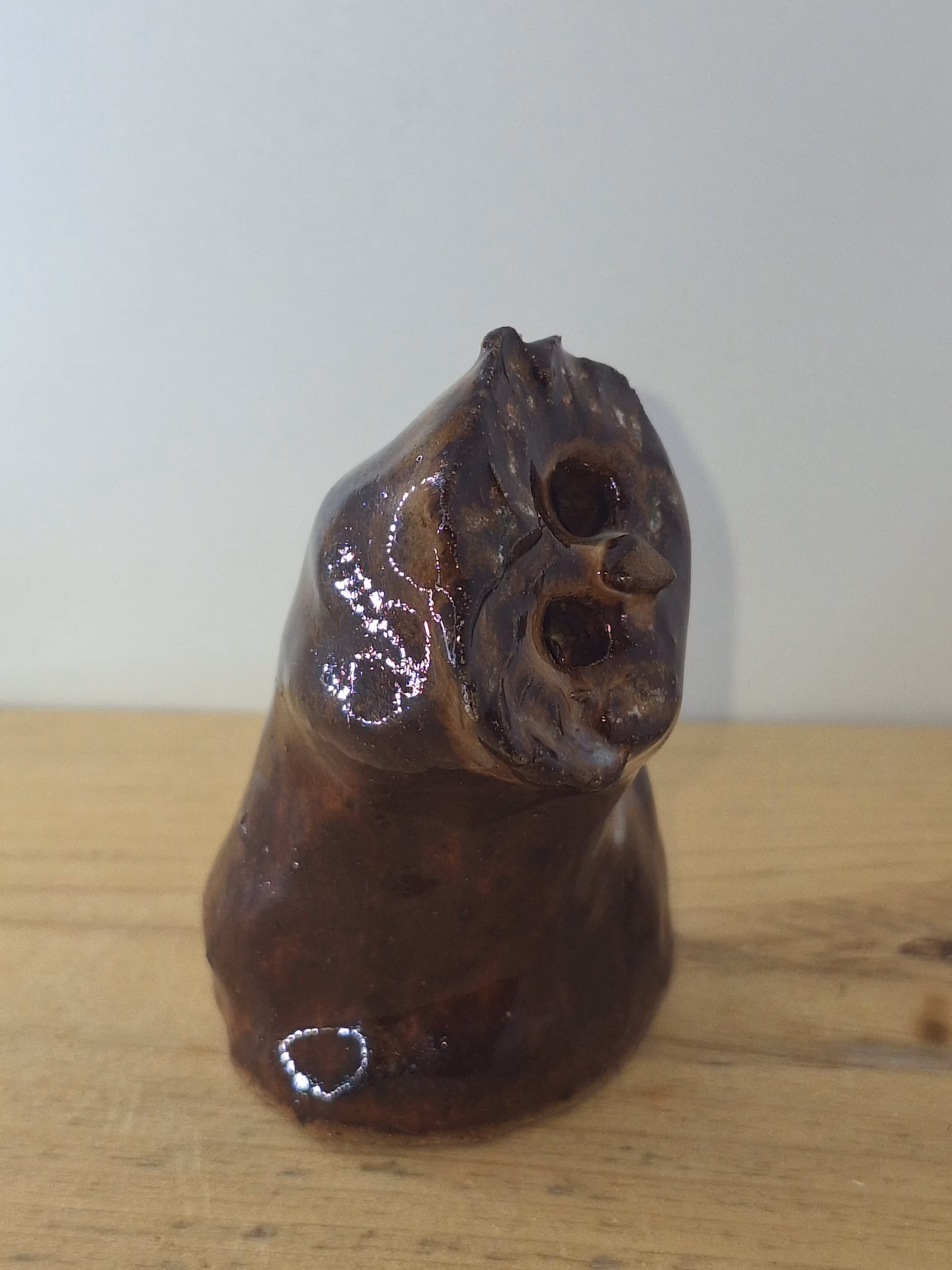 small ceramic owlet with dark brown glaze, head tilted thoughtfully, textured feather detail across face and body.