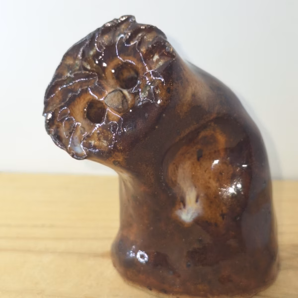 small ceramic owlet with dark brown glaze, head tilted thoughtfully, textured feather detail across face and body.
