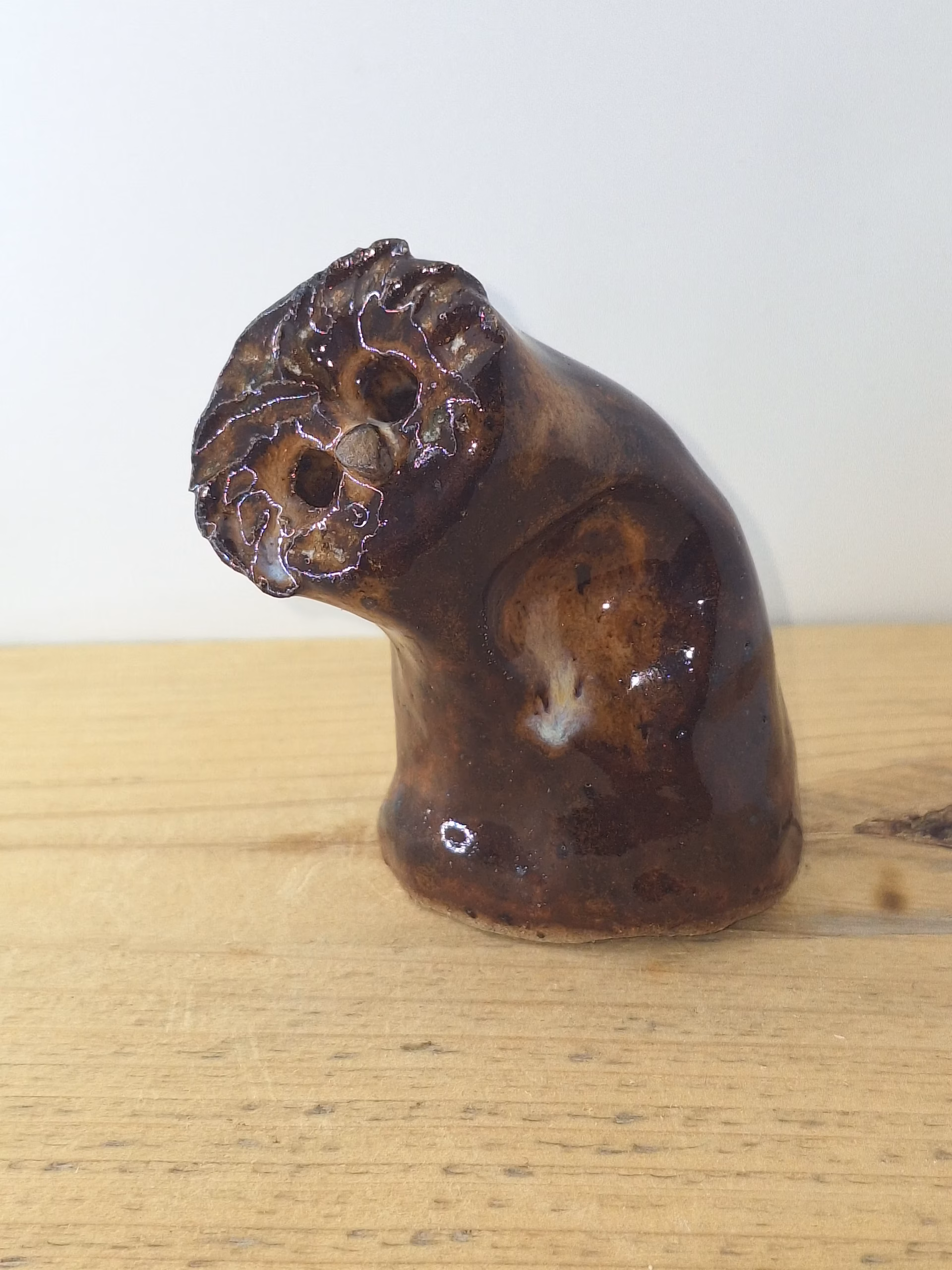 small ceramic owlet with dark brown glaze, head tilted thoughtfully, textured feather detail across face and body.