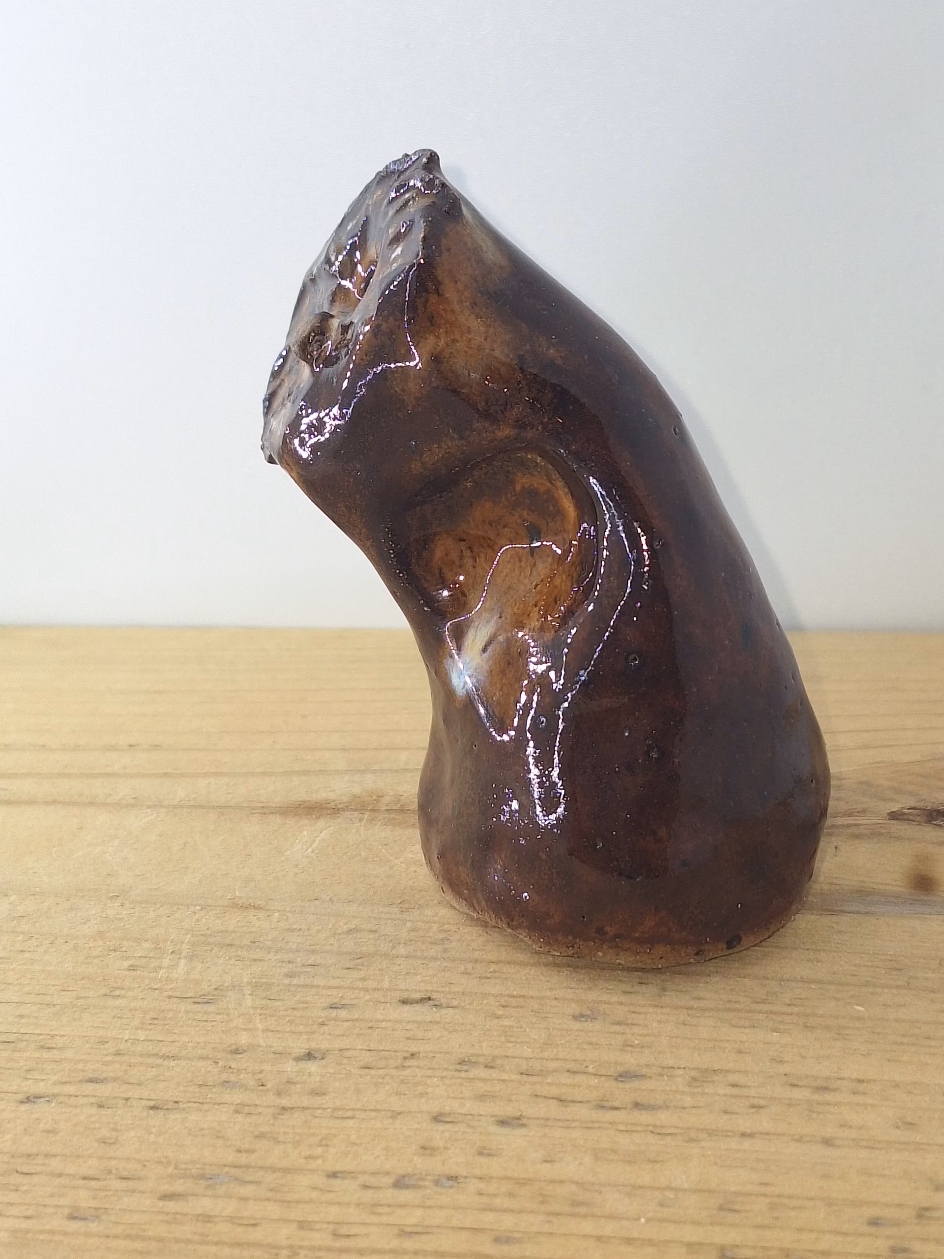 small ceramic owlet with dark brown glaze, head tilted thoughtfully, textured feather detail across face and body.