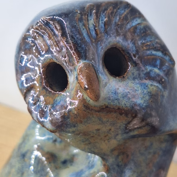 Small ceramic owlet with round head, dark hollow eyes, painted beak and feather detail in blue and brown tones.