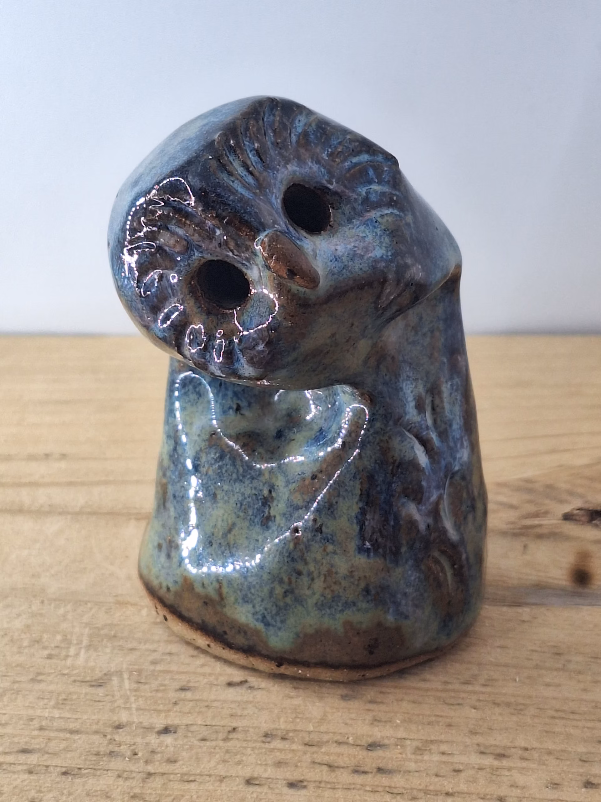 Small ceramic owlet with round head, dark hollow eyes, painted beak and feather detail in blue and brown tones.