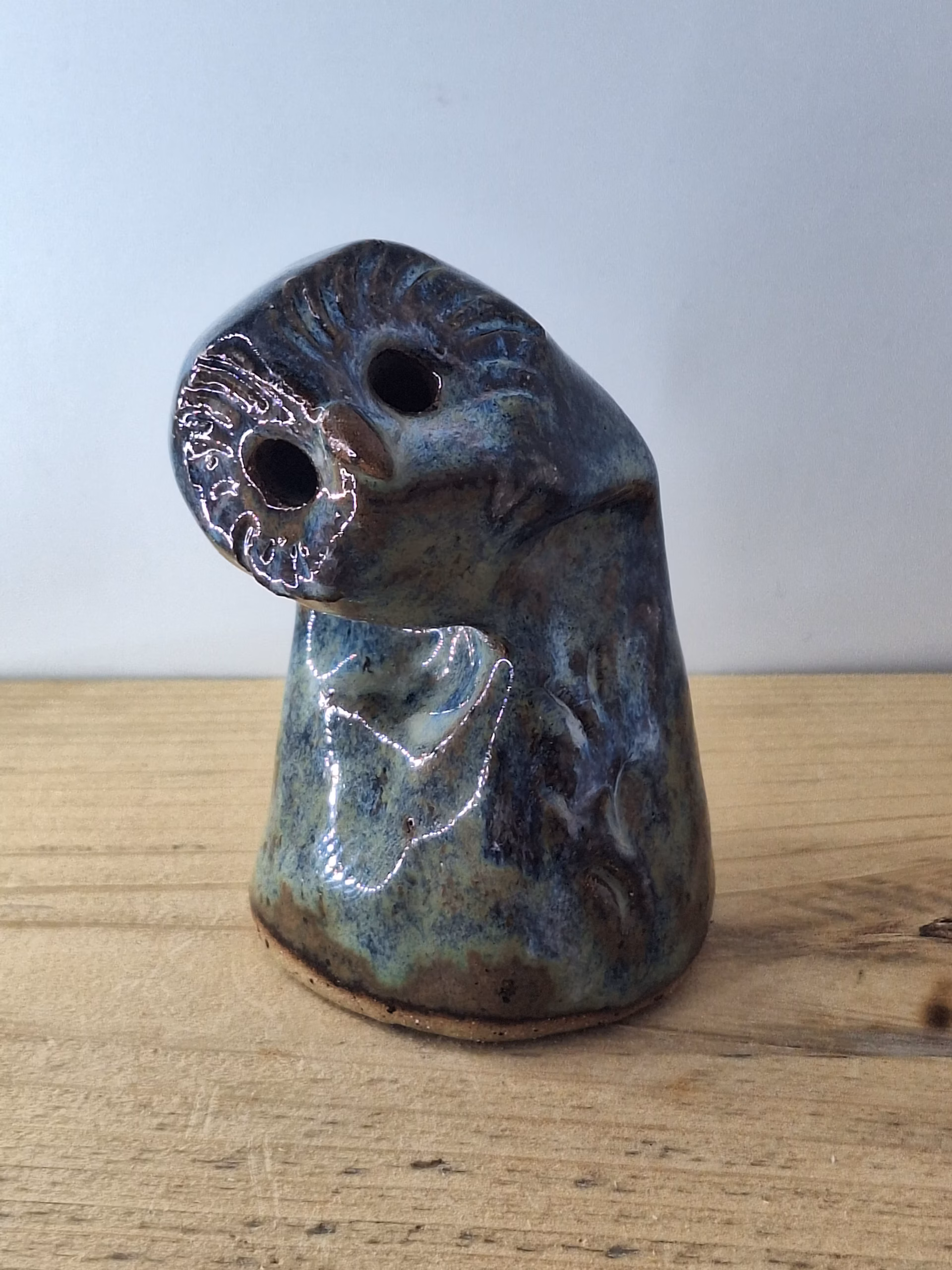 Small ceramic owlet with round head, dark hollow eyes, painted beak and feather detail in blue and brown tones.