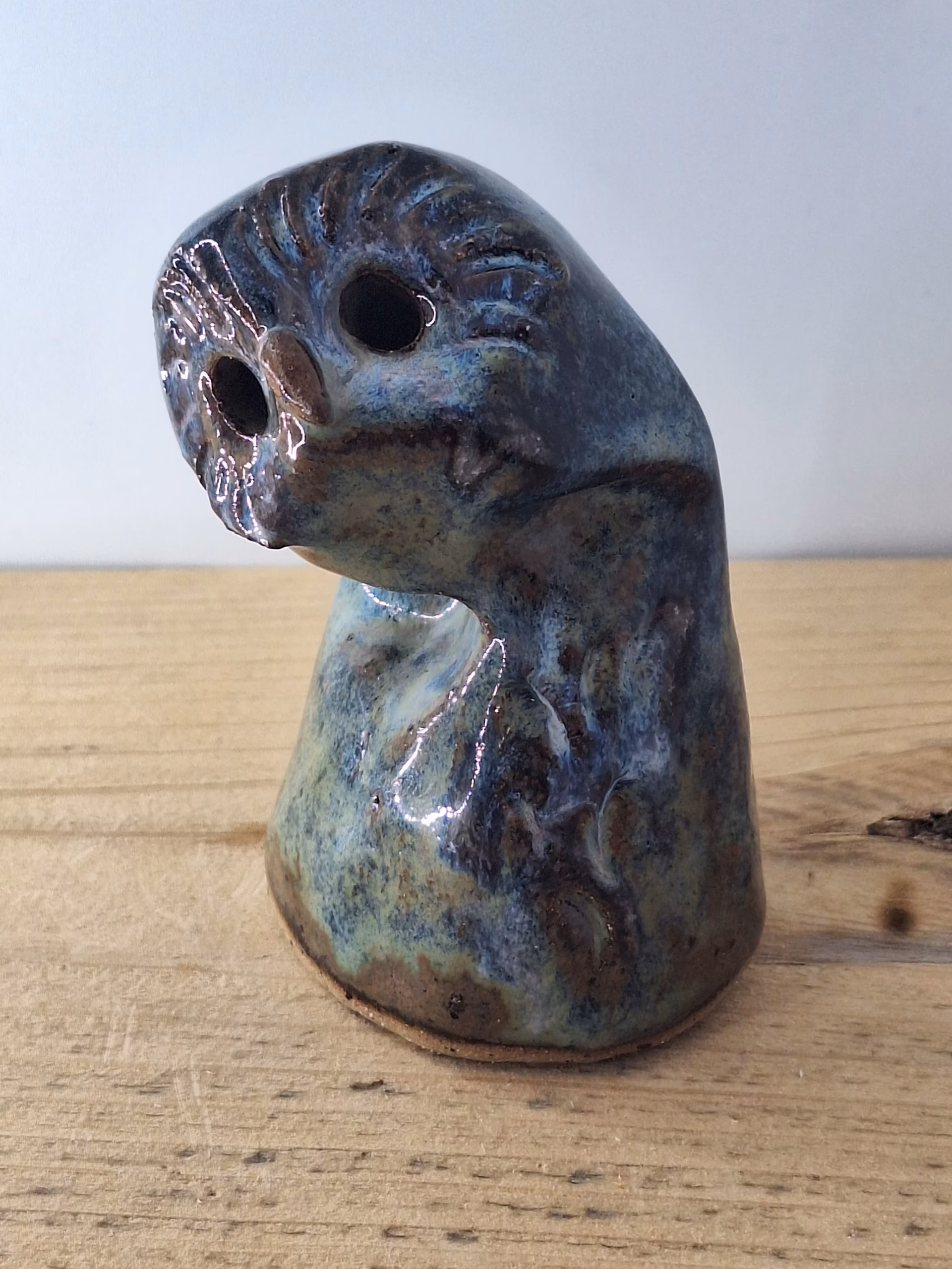 Small ceramic owlet with round head, dark hollow eyes, painted beak and feather detail in blue and brown tones.