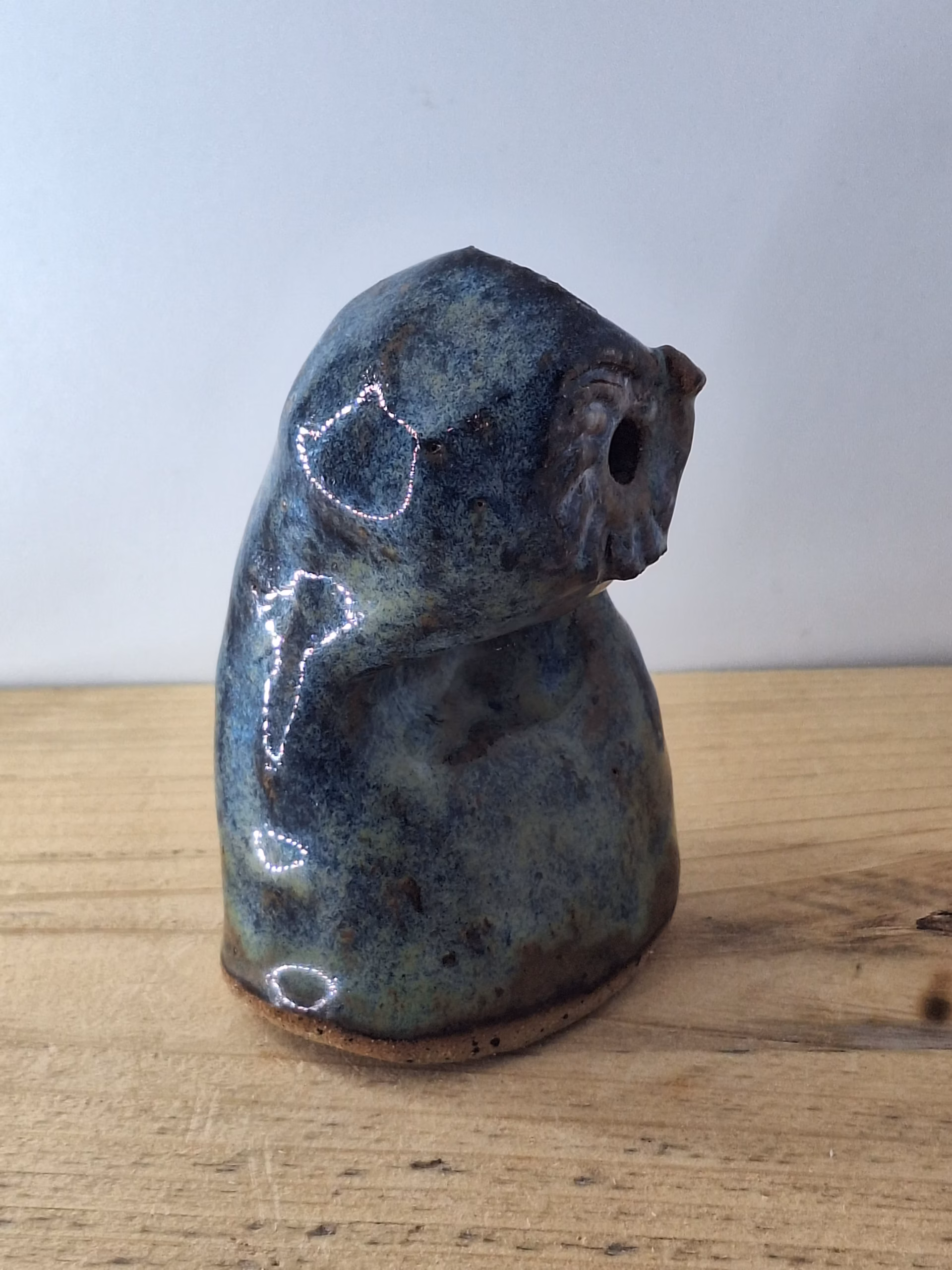 Small ceramic owlet with round head, dark hollow eyes, painted beak and feather detail in blue and brown tones.