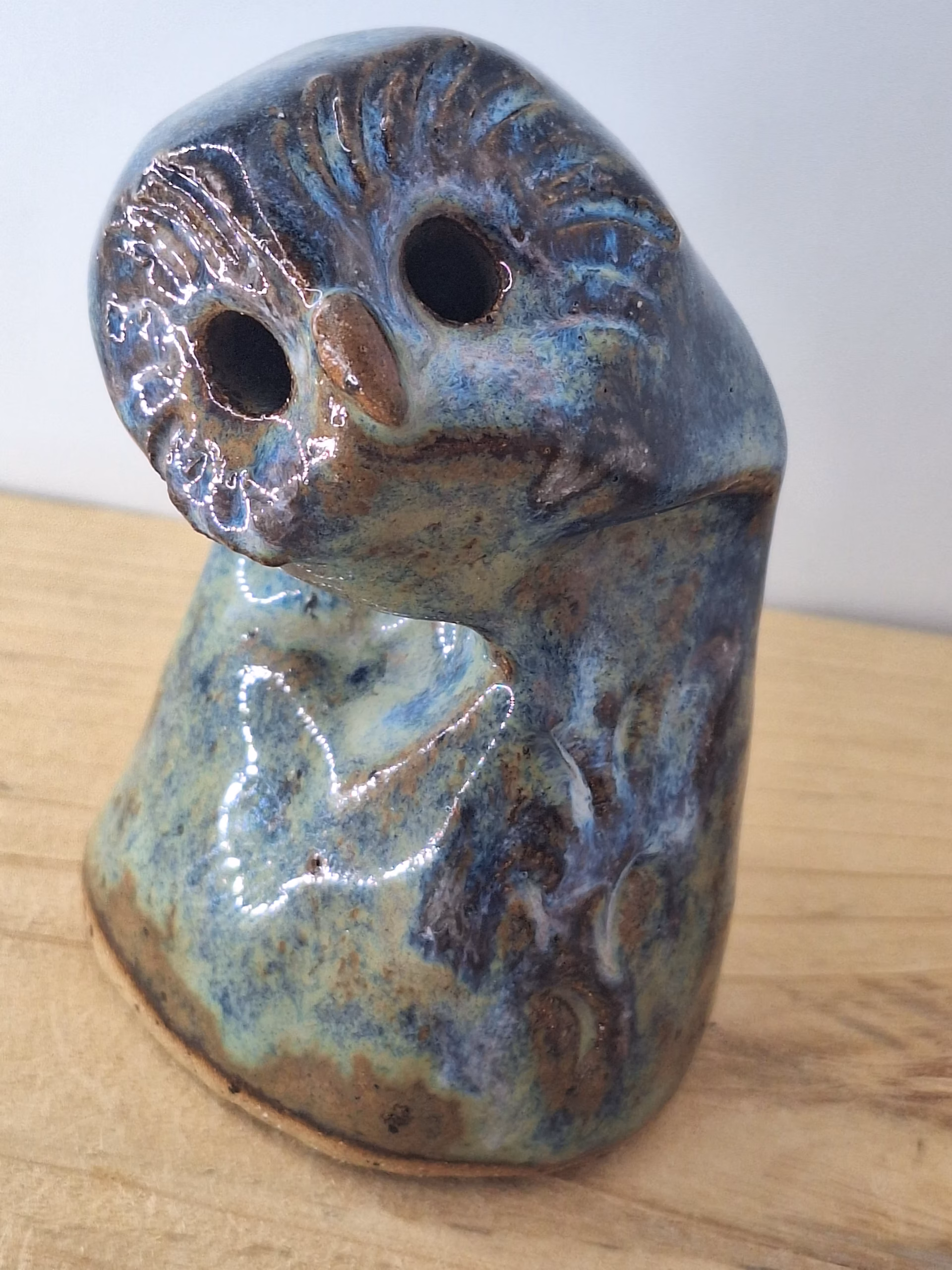 Small ceramic owlet with round head, dark hollow eyes, painted beak and feather detail in blue and brown tones.