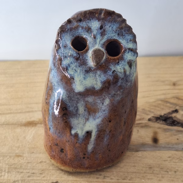 Small ceramic owl figurine with round body, large dark eyes, and mottled blue-brown painted surface.