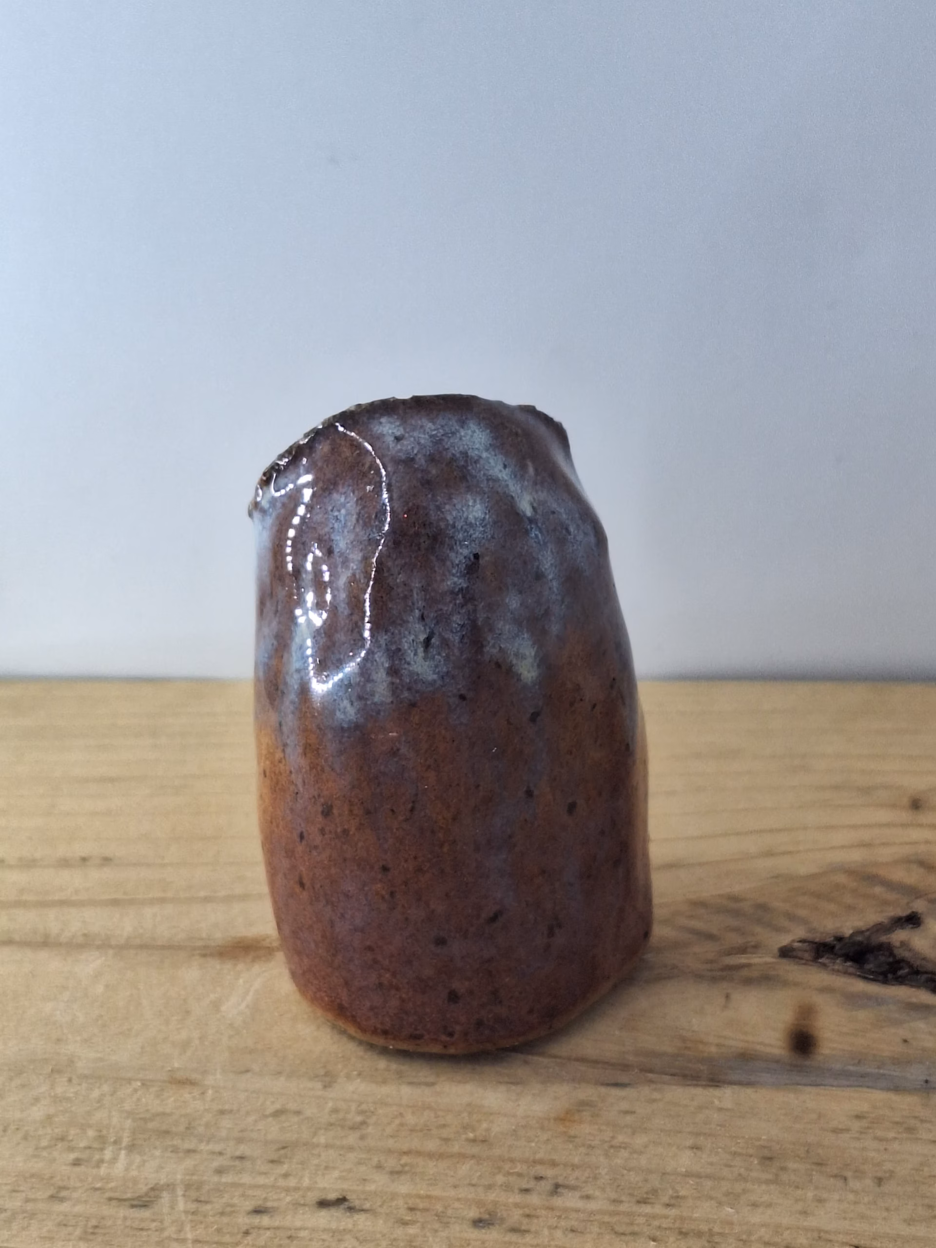 Small ceramic owl figurine with round body, large dark eyes, and mottled blue-brown painted surface.