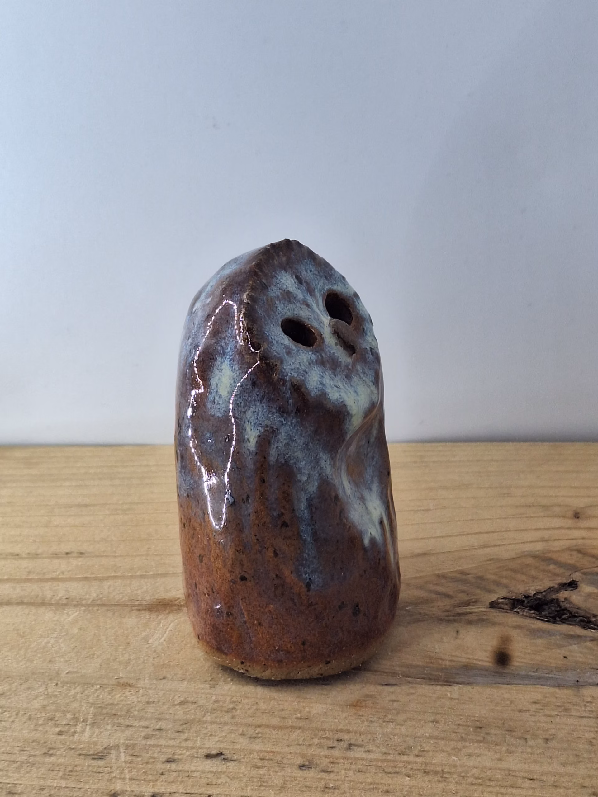 Small ceramic owl figurine with round body, large dark eyes, and mottled blue-brown painted surface.
