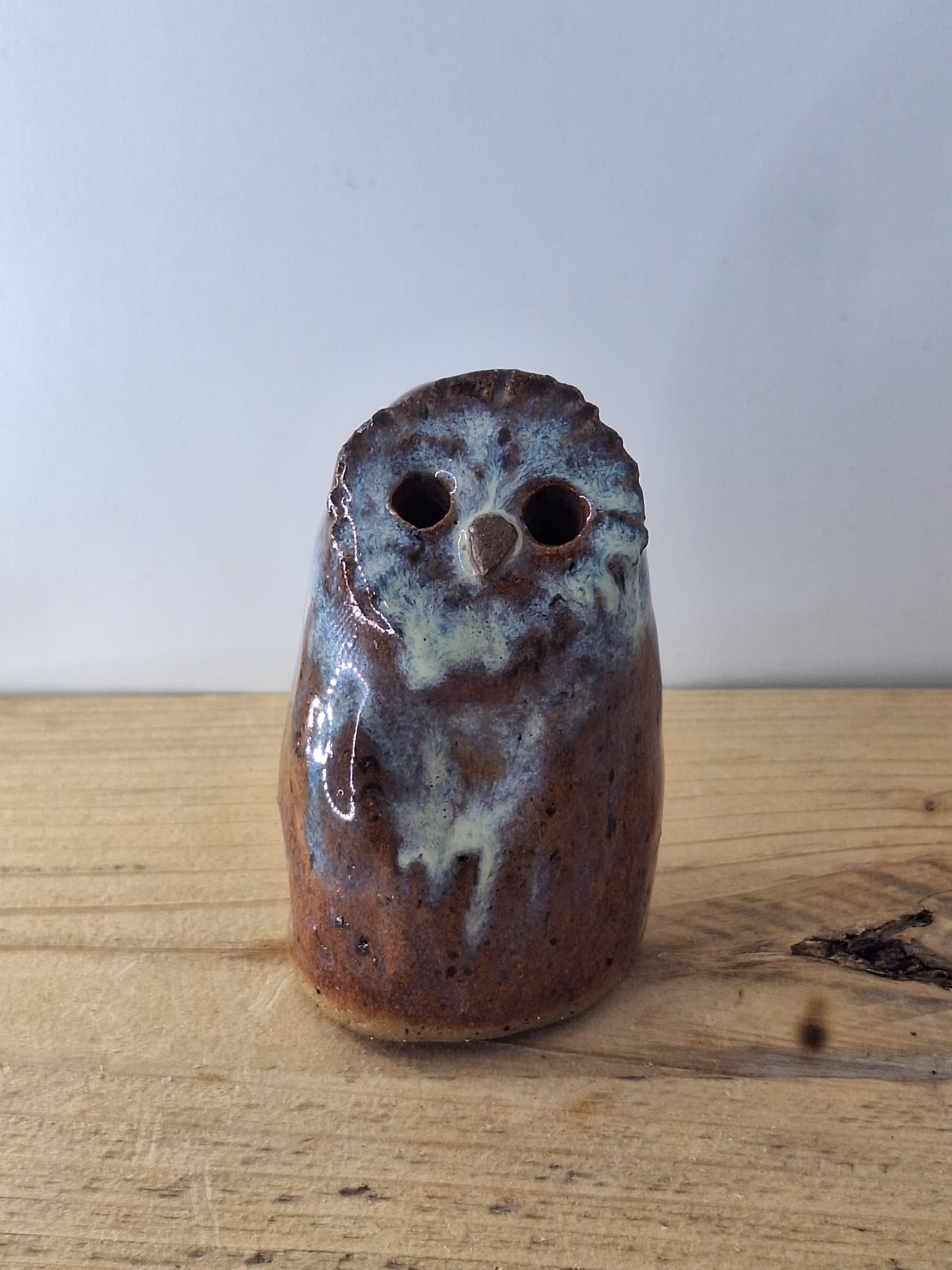 Small ceramic owl figurine with round body, large dark eyes, and mottled blue-brown painted surface.