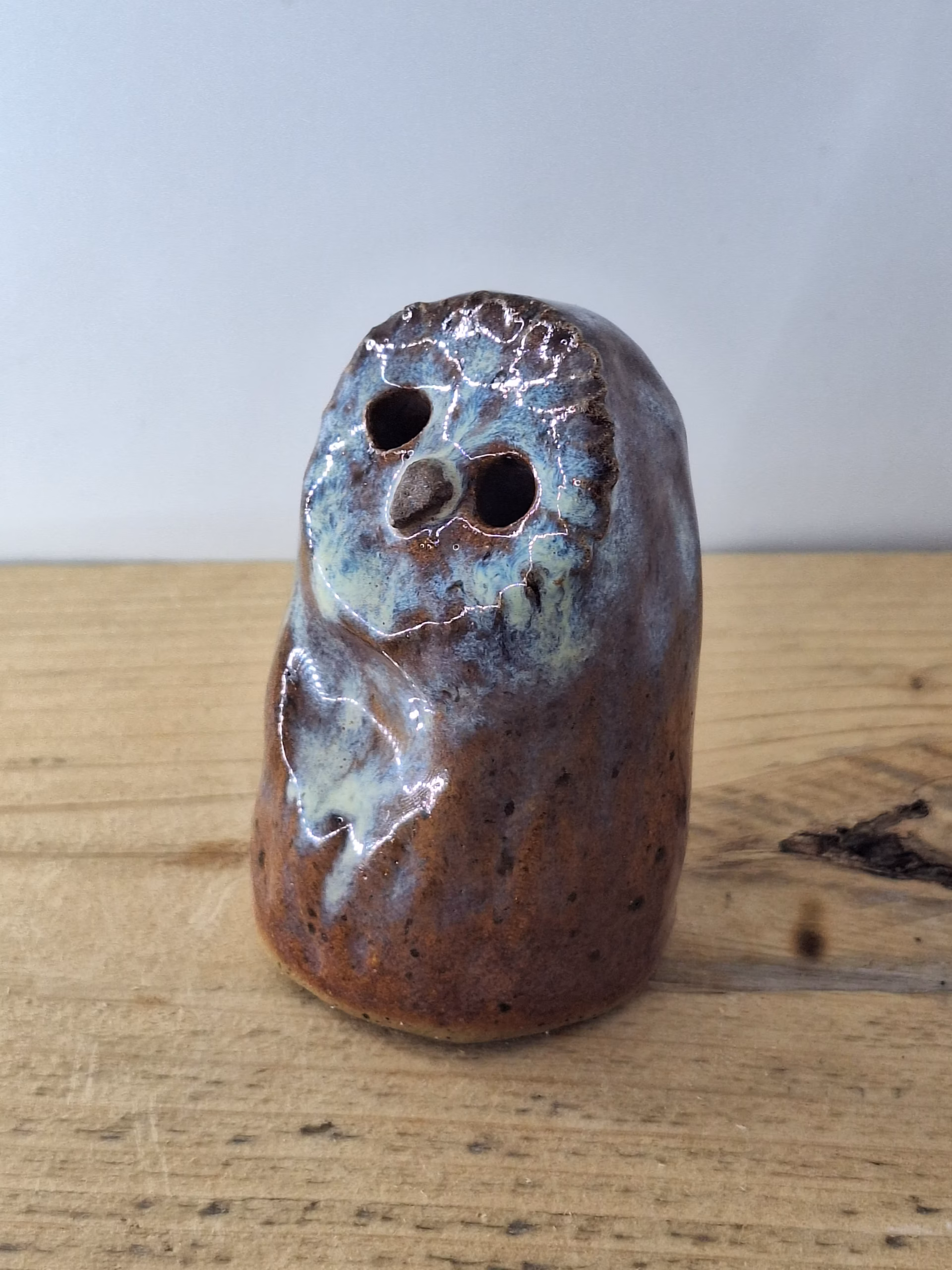 Small ceramic owl figurine with round body, large dark eyes, and mottled blue-brown painted surface.