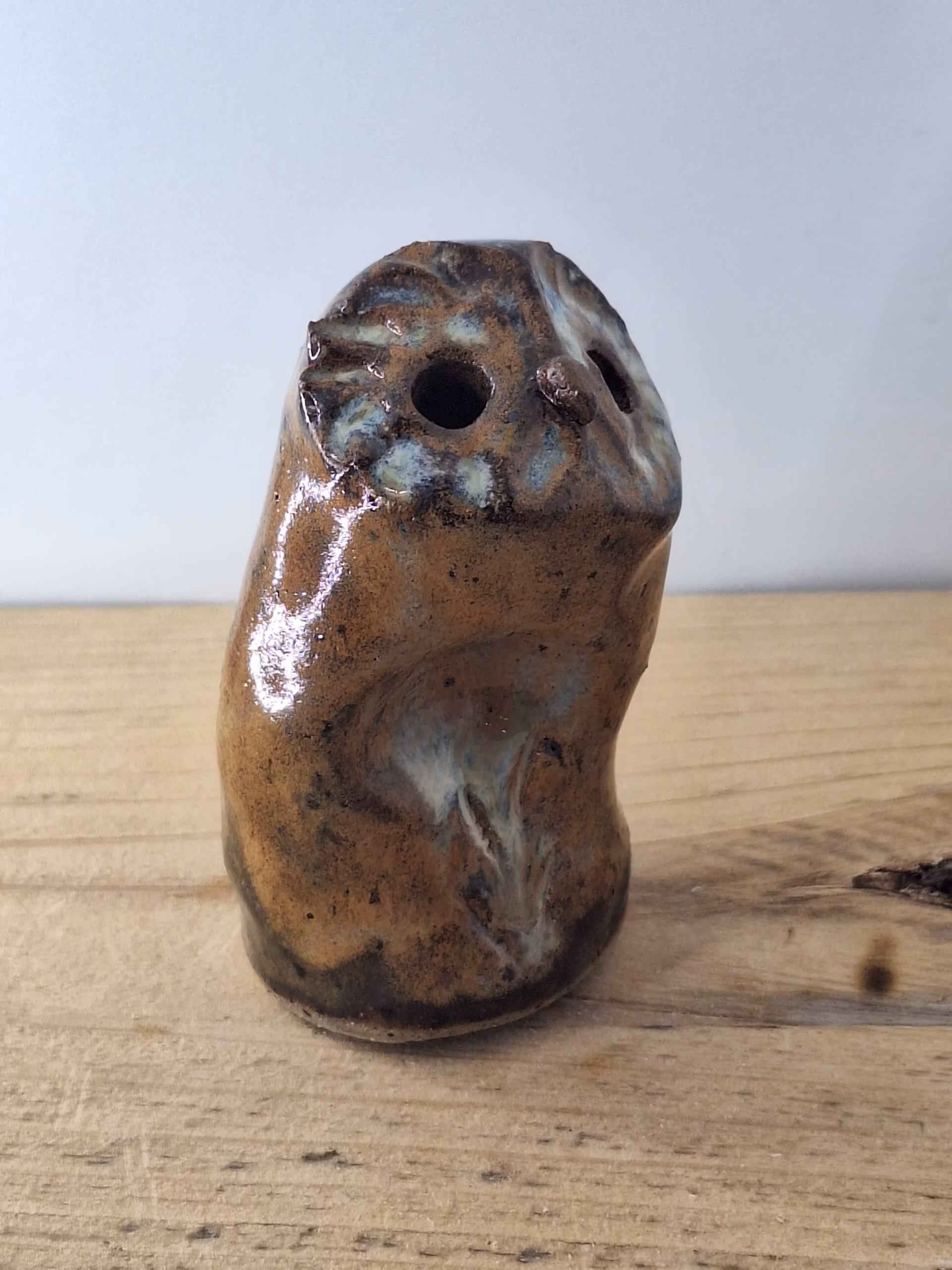 Small ceramic owl figurine with mottled brown and blue glaze, round head with large circular eyes and textured surface.