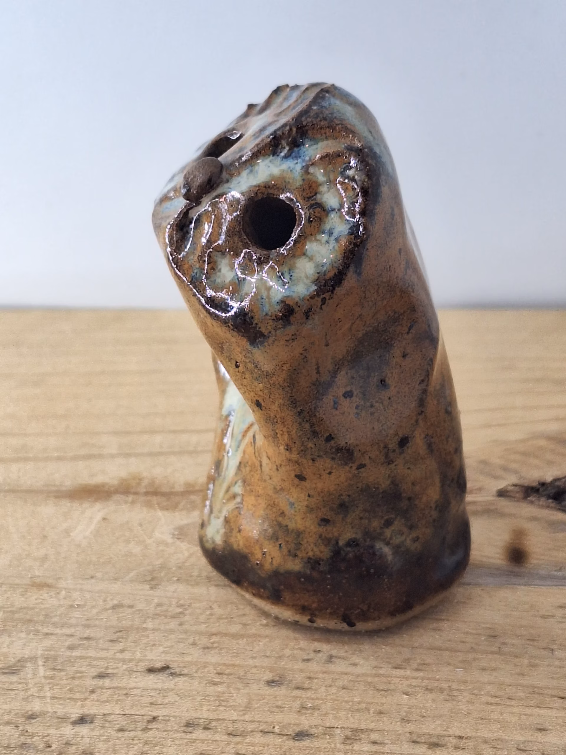 Small ceramic owl figurine with mottled brown and blue glaze, round head with large circular eyes and textured surface.