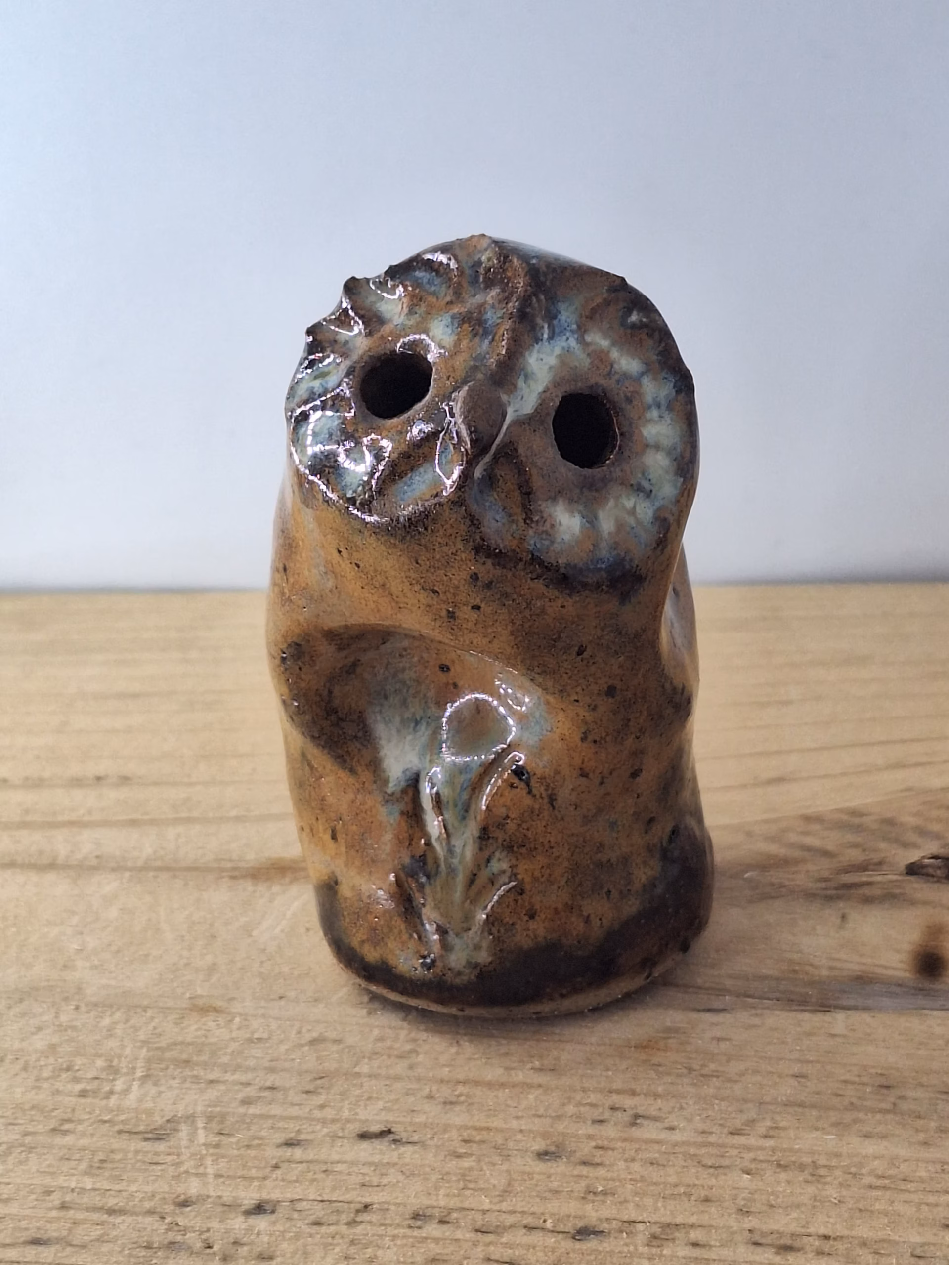 Small ceramic owl figurine with mottled brown and blue glaze, round head with large circular eyes and textured surface.