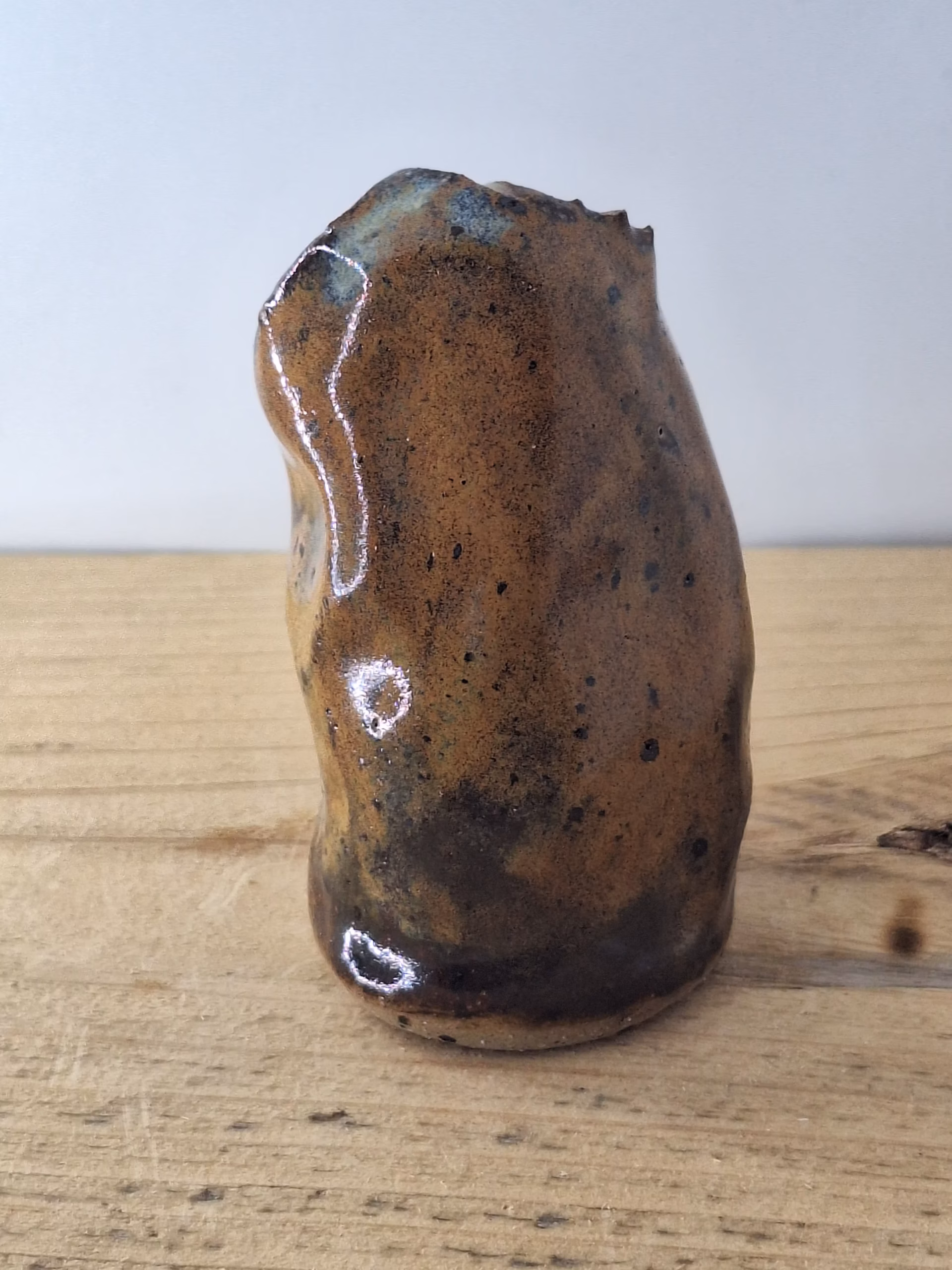 Small ceramic owl figurine with mottled brown and blue glaze, round head with large circular eyes and textured surface.