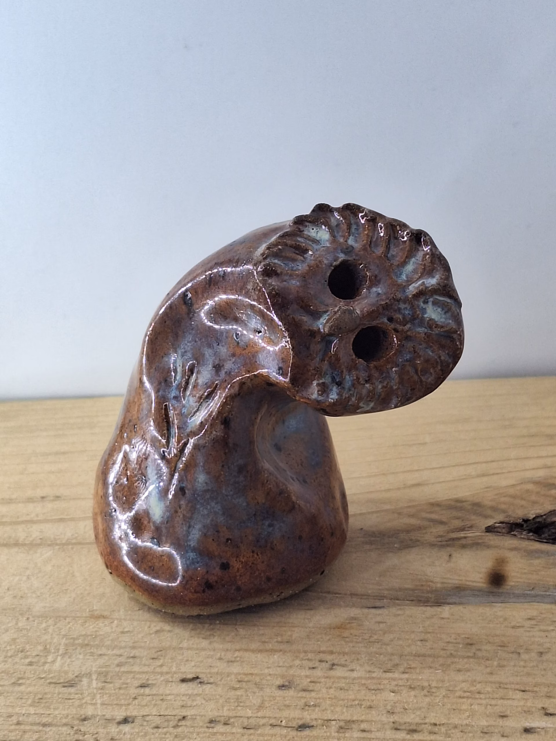 Small ceramic owl with textured feather detail, warm brown tones and blue-grey accents, two round eye holes.
