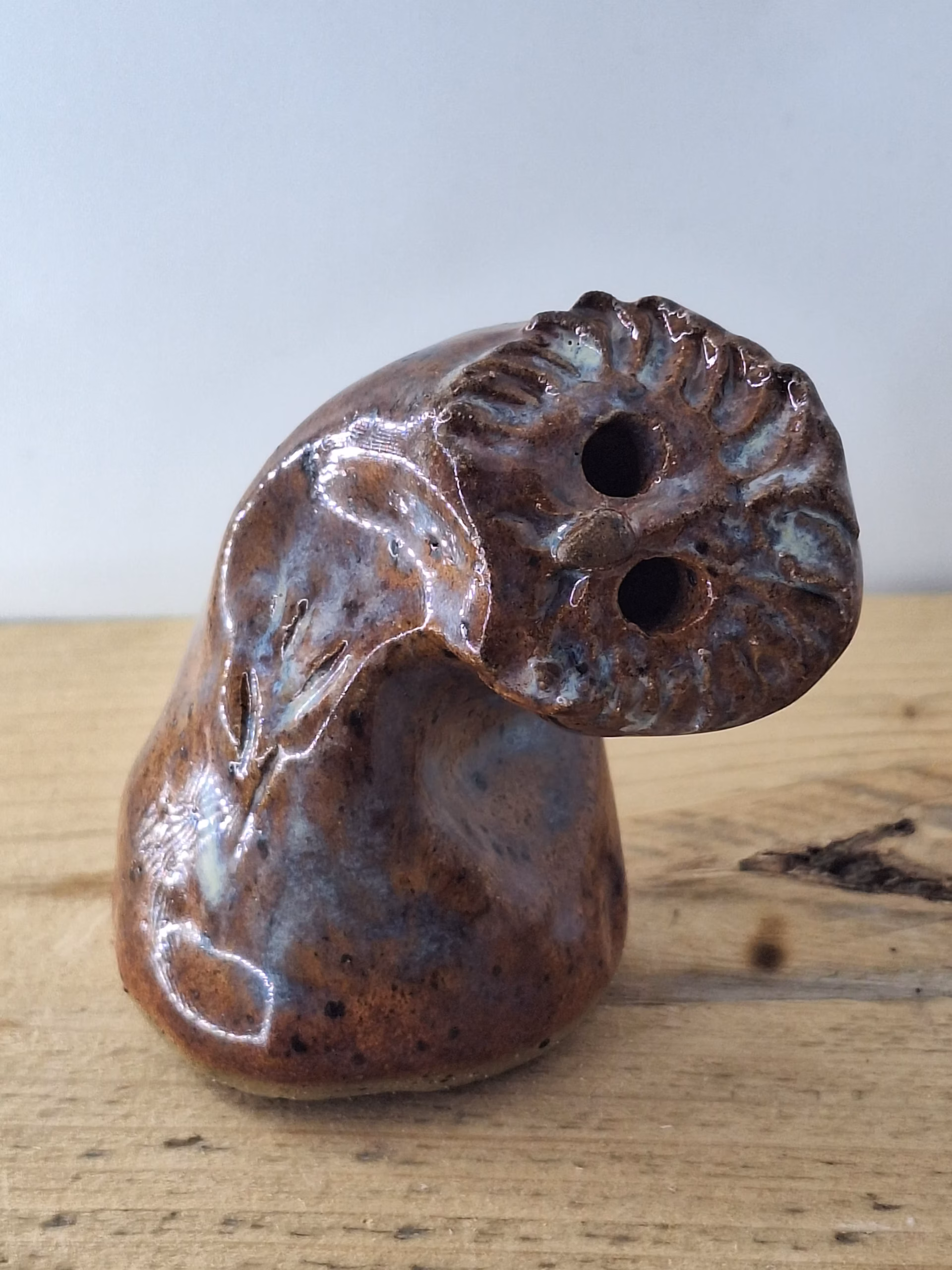 Small ceramic owl with textured feather detail, warm brown tones and blue-grey accents, two round eye holes.