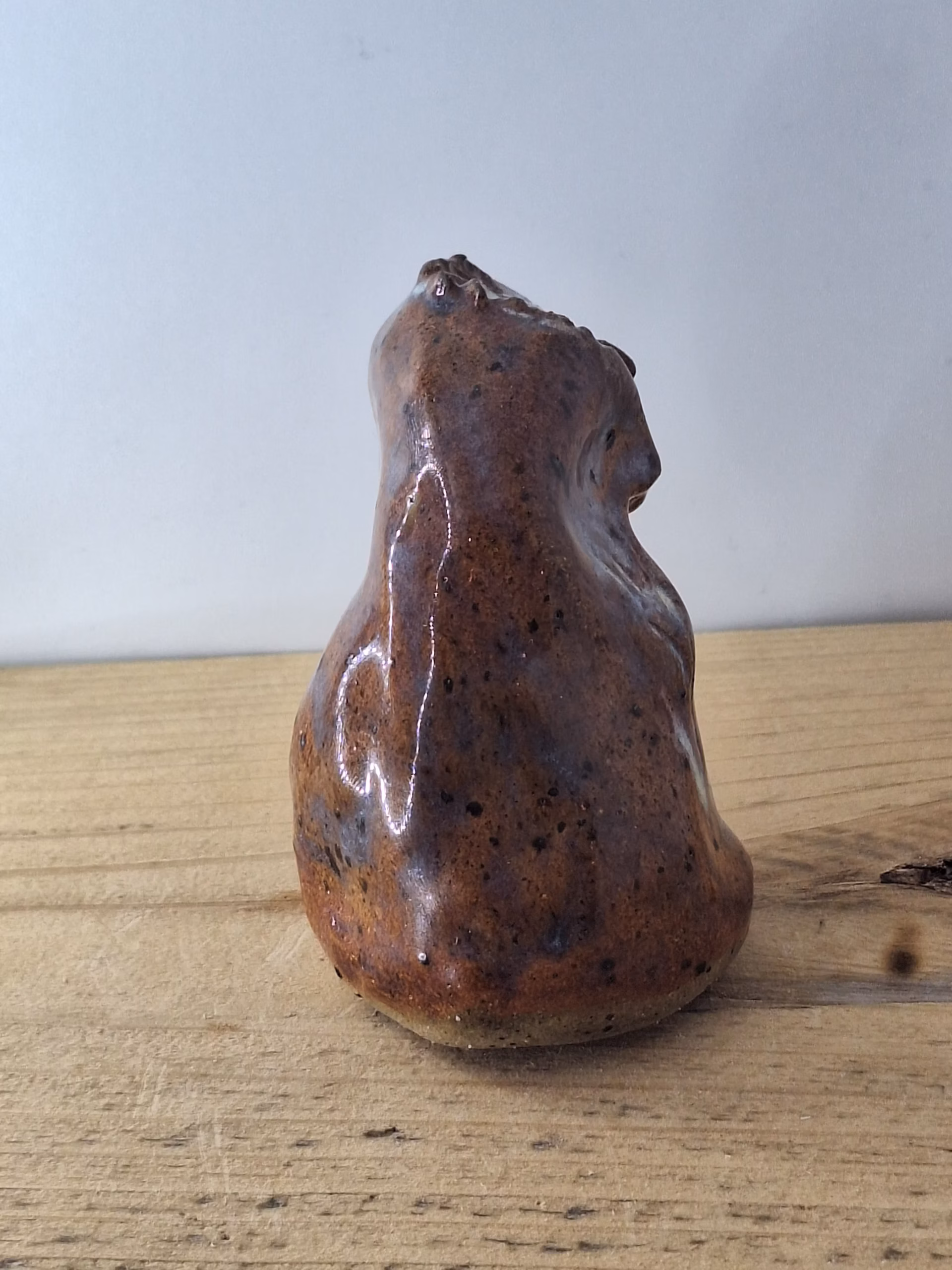 Small ceramic owl with textured feather detail, warm brown tones and blue-grey accents, two round eye holes.