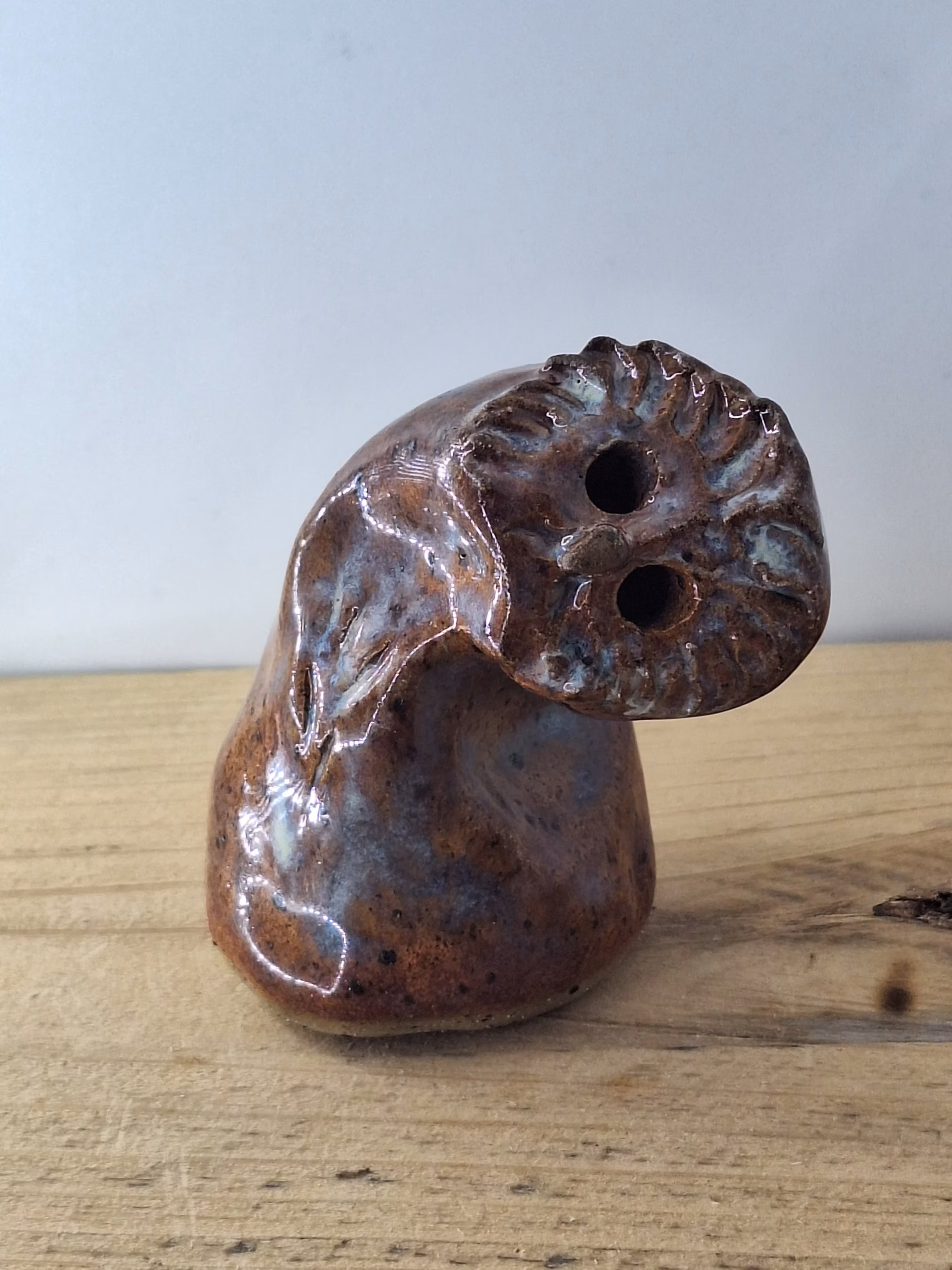 Small ceramic owl with textured feather detail, warm brown tones and blue-grey accents, two round eye holes.