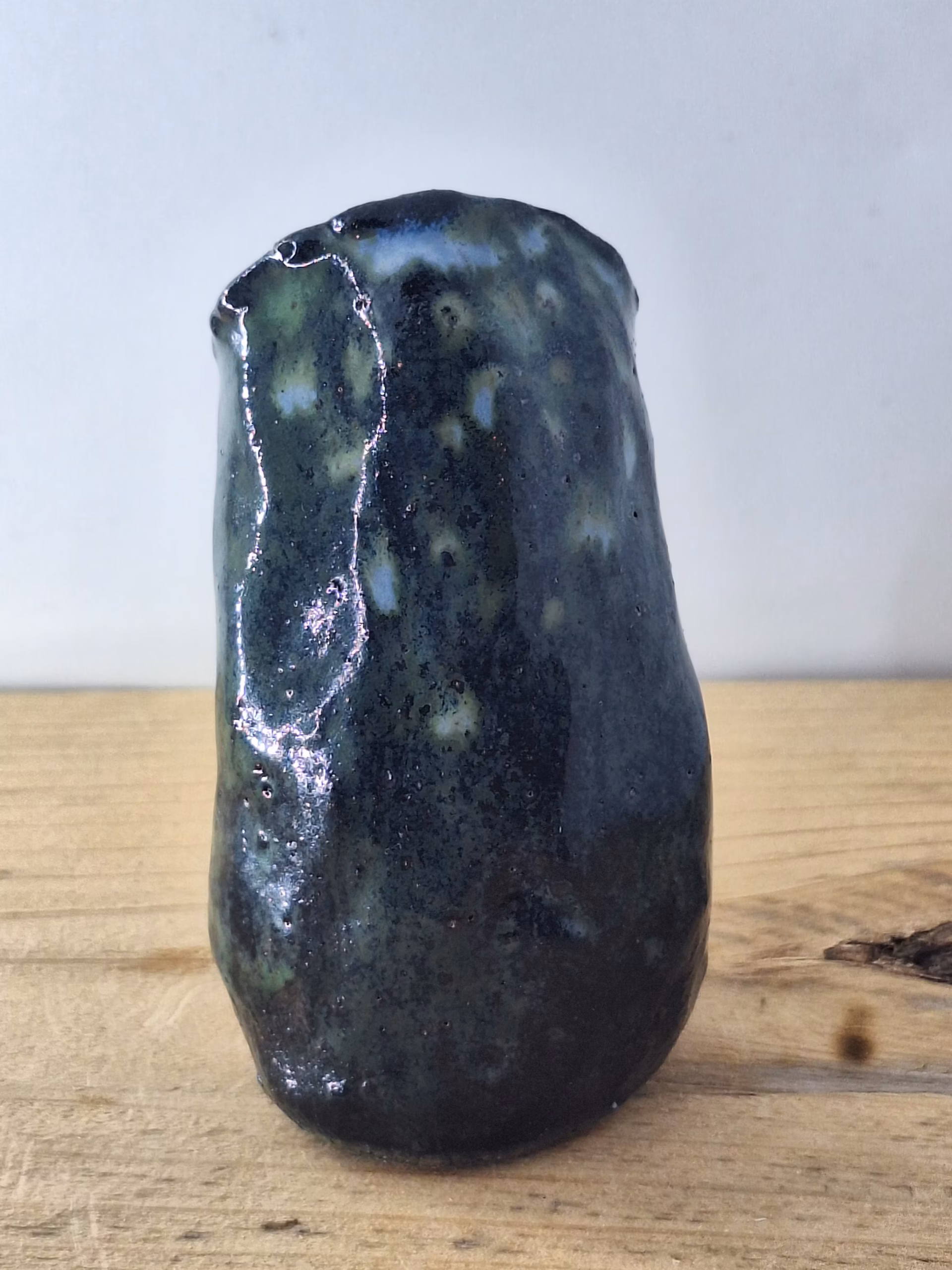 Small ceramic owl with large round eyes, mottled blue and green surface, and a tiny spider perched on its chest.