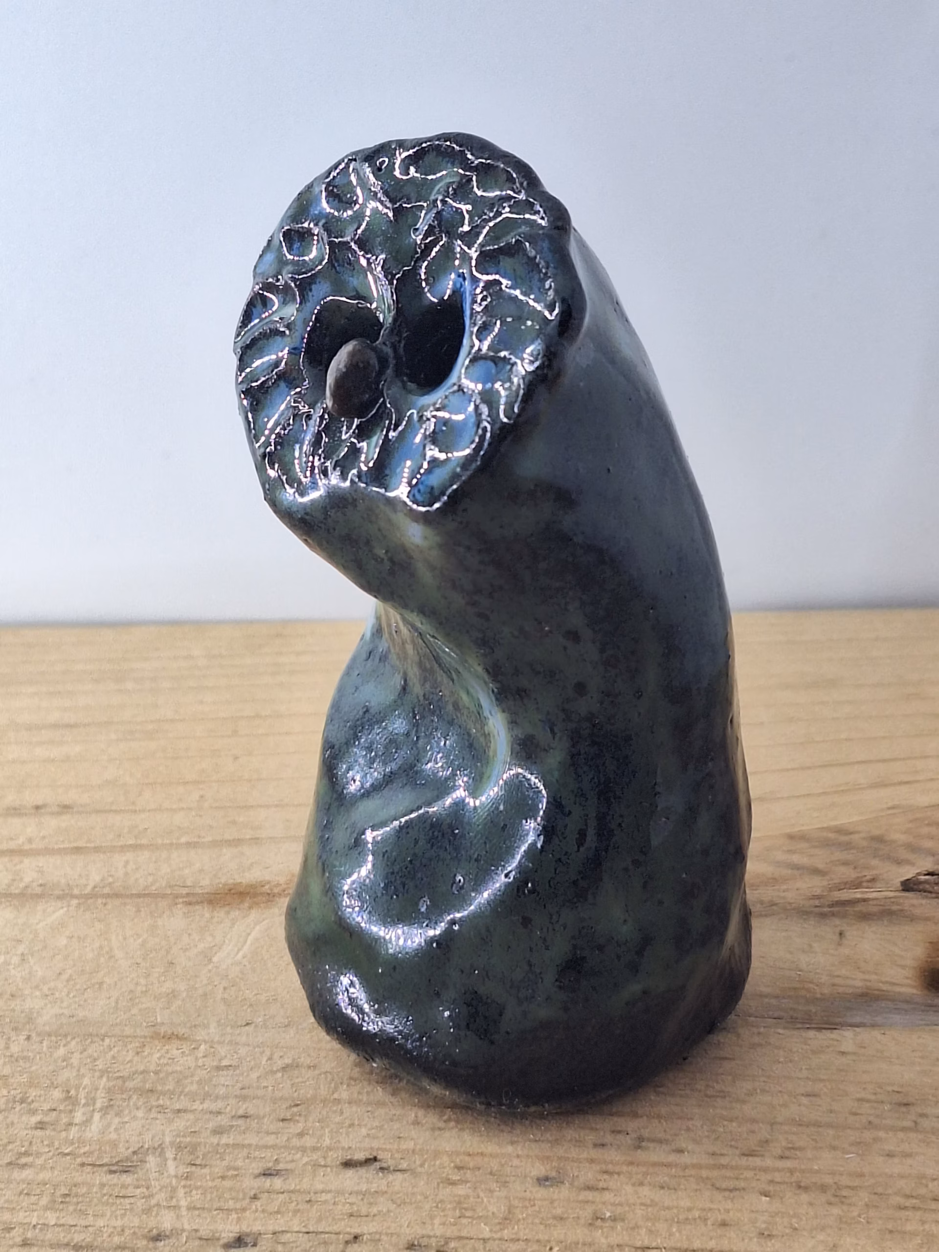 Small ceramic owl with large round eyes, mottled blue and green surface, and a tiny spider perched on its chest.