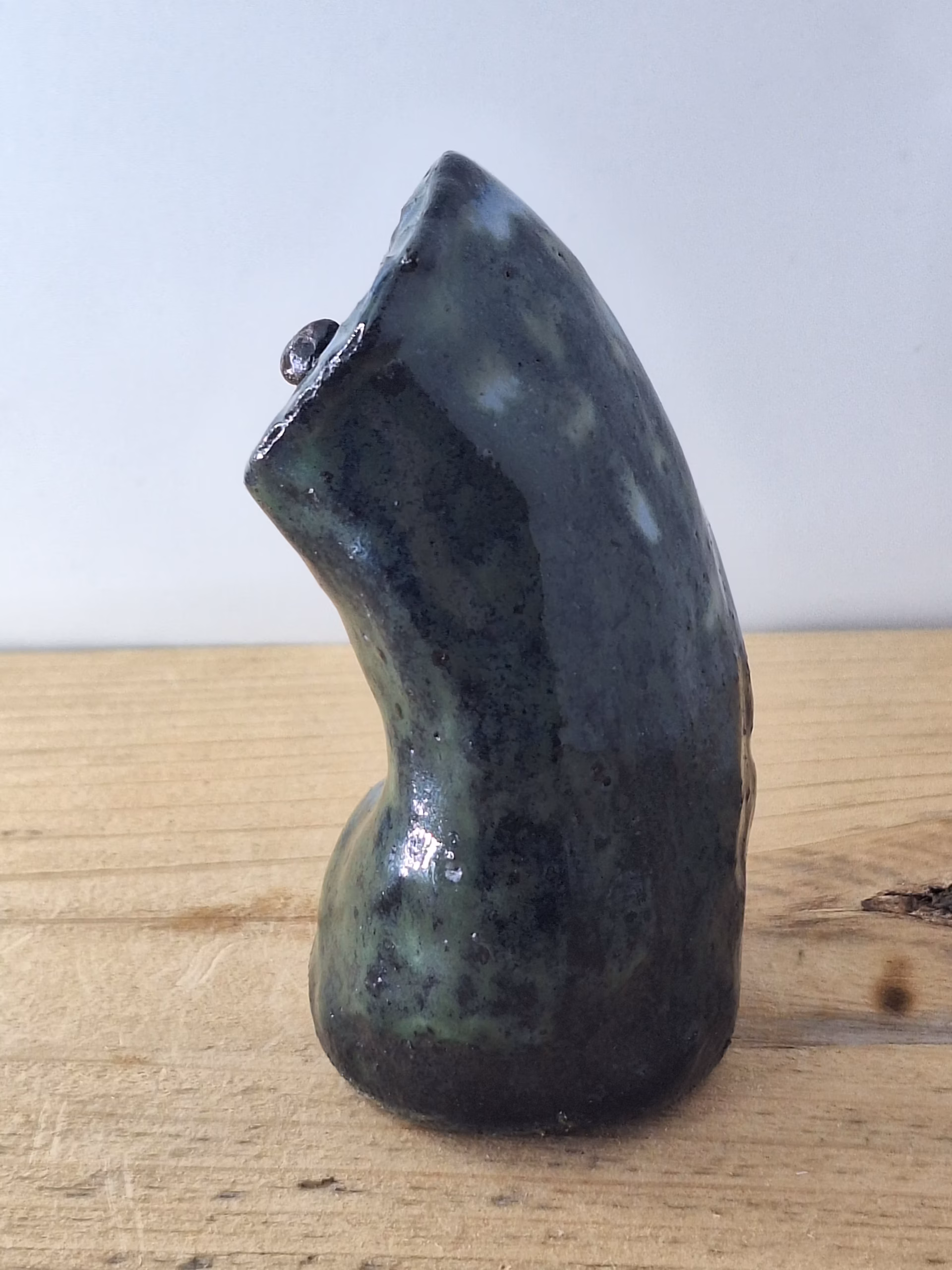 Small ceramic owl with large round eyes, mottled blue and green surface, and a tiny spider perched on its chest.