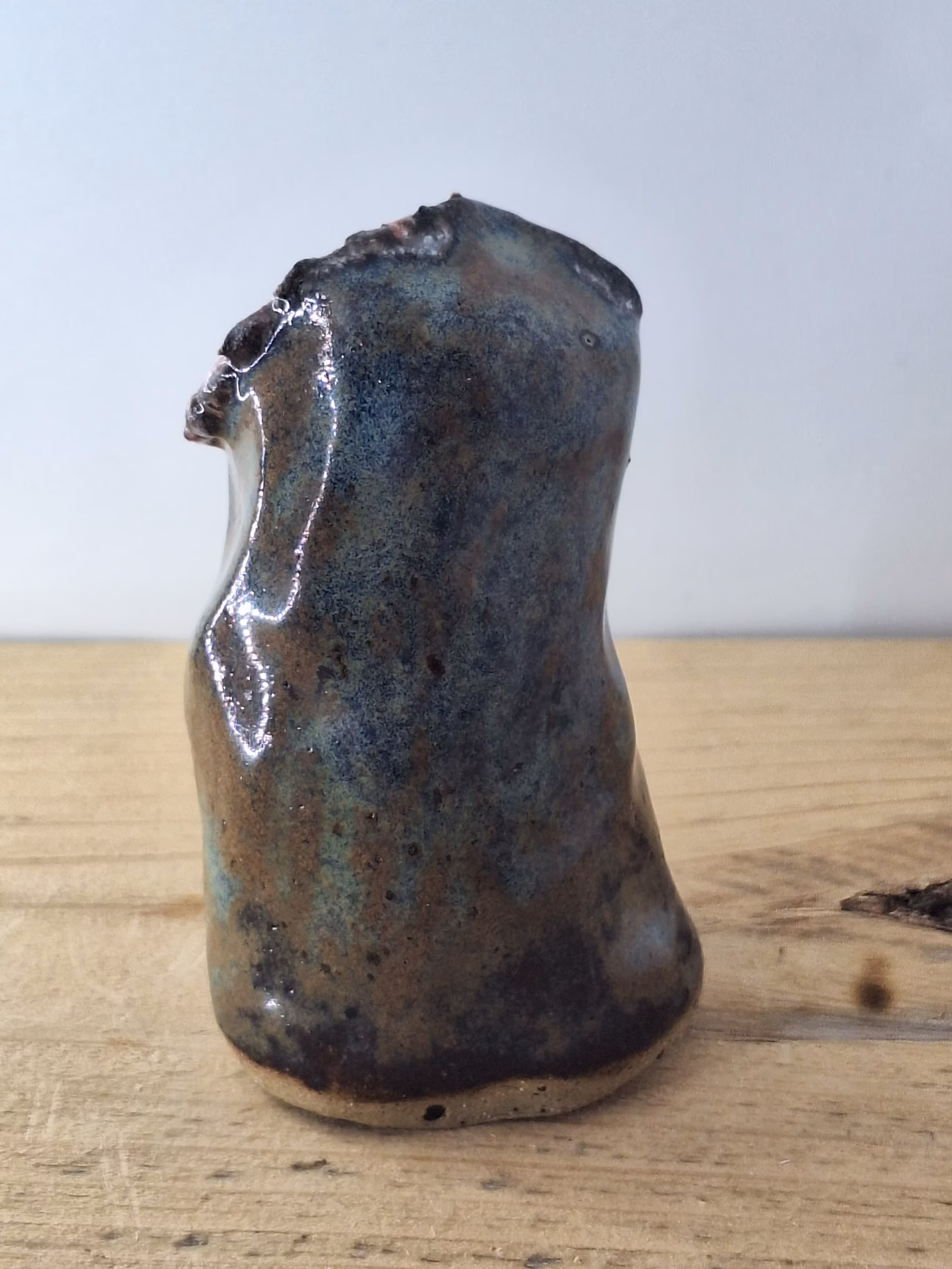 small ceramic owl head with textured pink and blue surface, dark round eyes, perched on a cylindrical base.