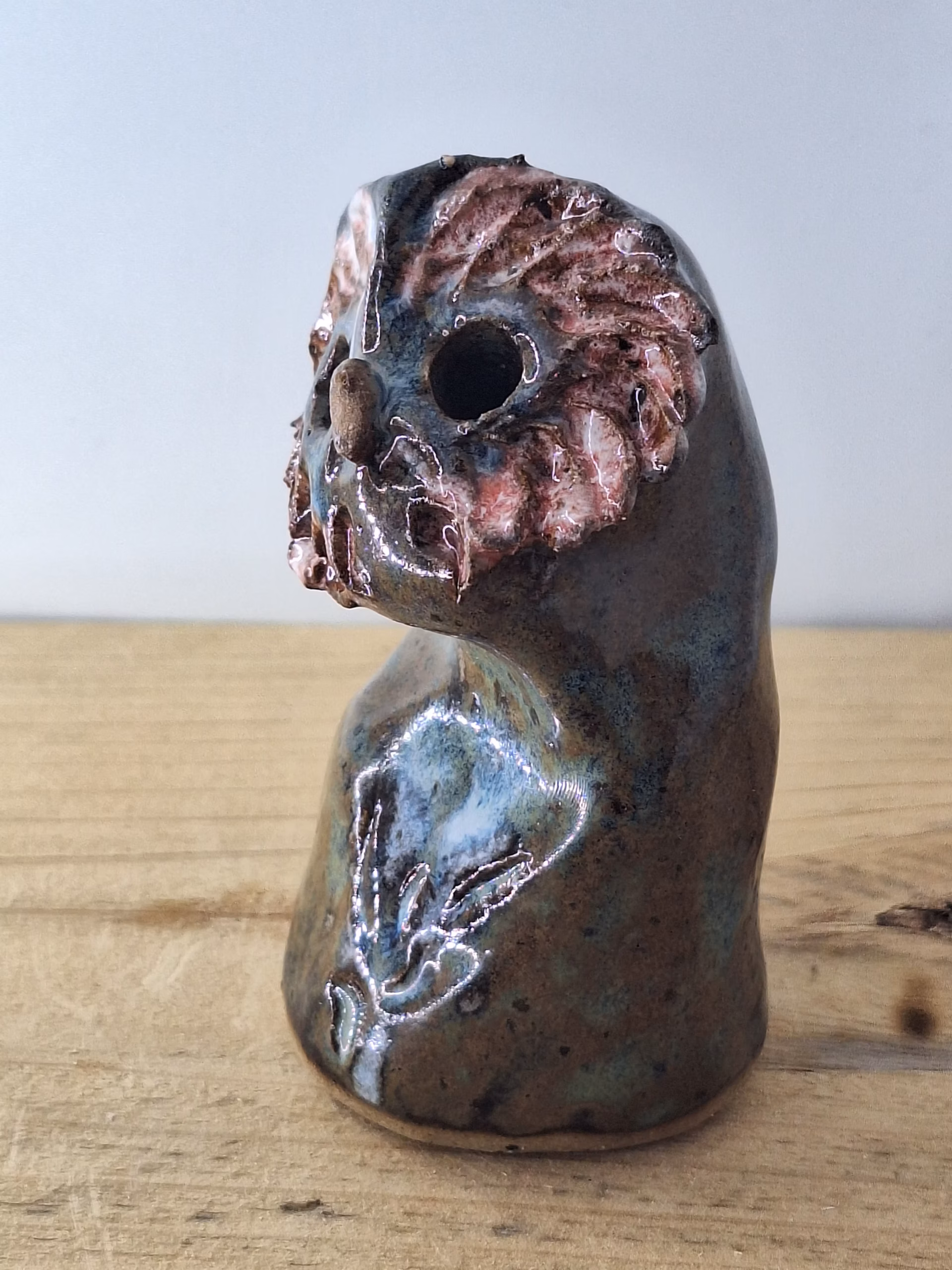 small ceramic owl head with textured pink and blue surface, dark round eyes, perched on a cylindrical base.