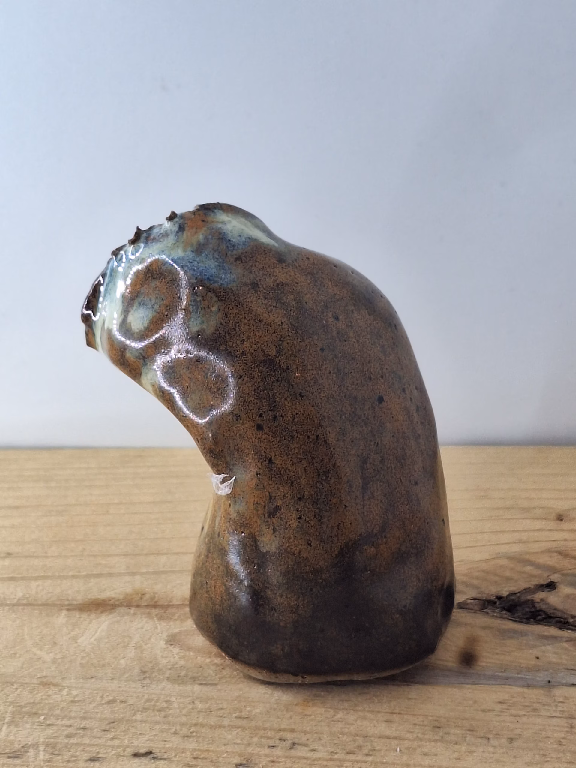 Small ceramic owl with a rounded body, textured surface in warm browns and creams, two dark hollow eyes, and a contemplative expression.