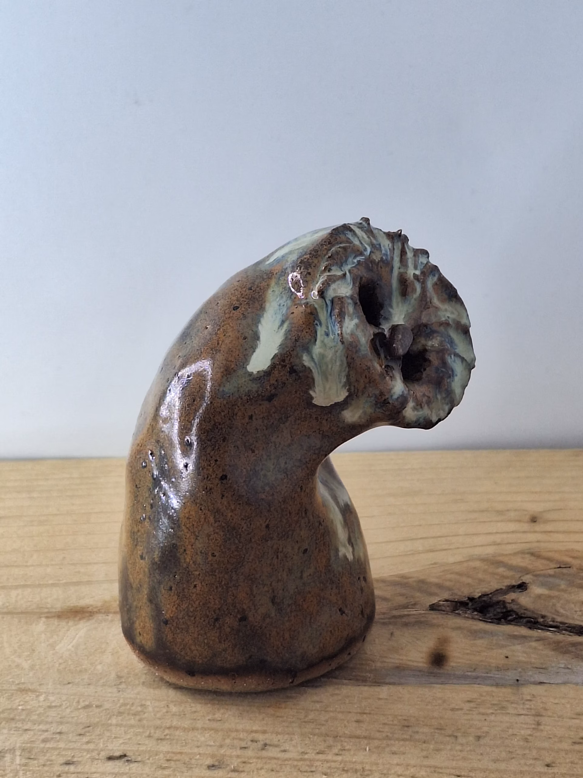Small ceramic owl with a rounded body, textured surface in warm browns and creams, two dark hollow eyes, and a contemplative expression.