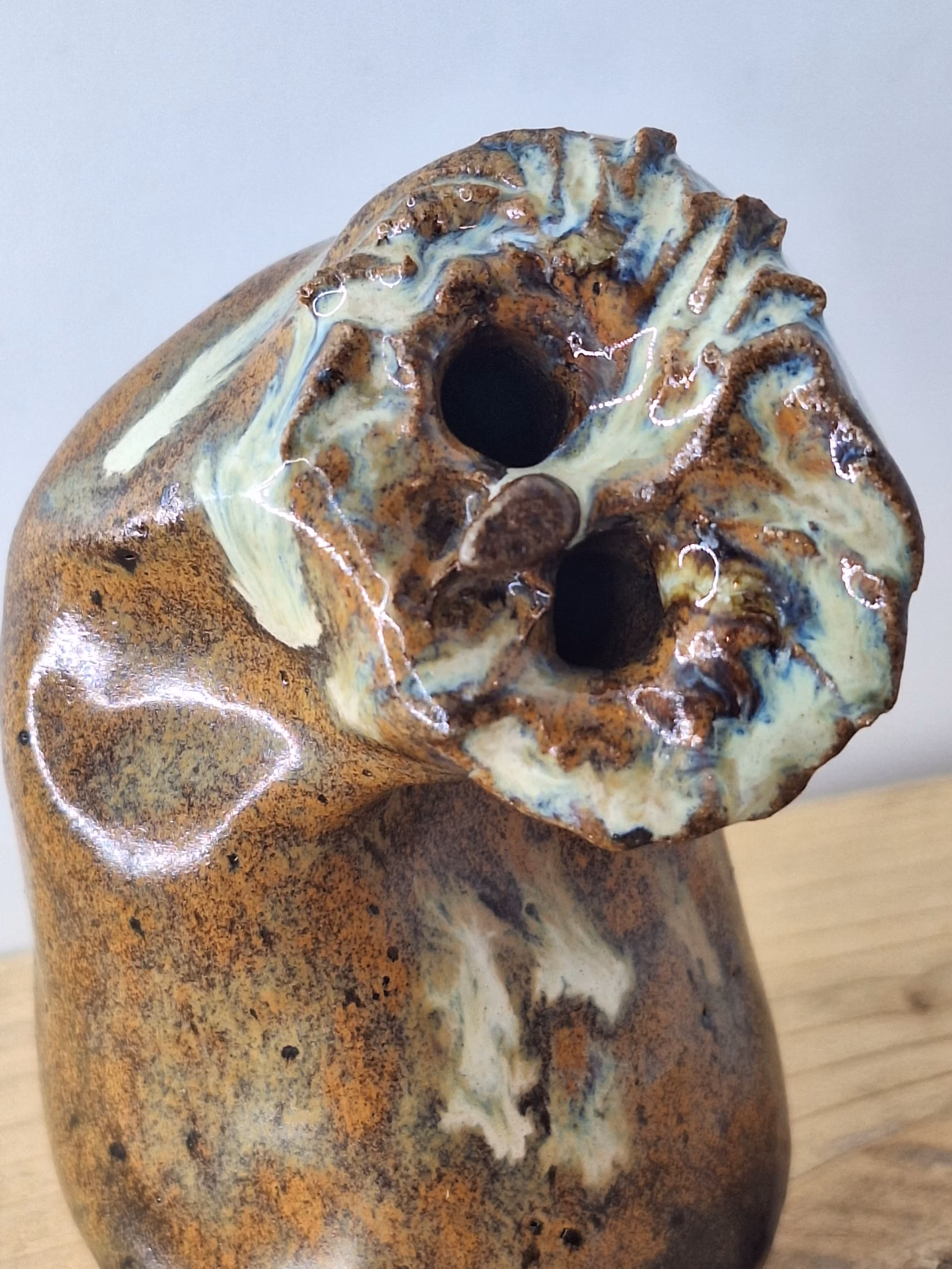 Small ceramic owl with a rounded body, textured surface in warm browns and creams, two dark hollow eyes, and a contemplative expression.