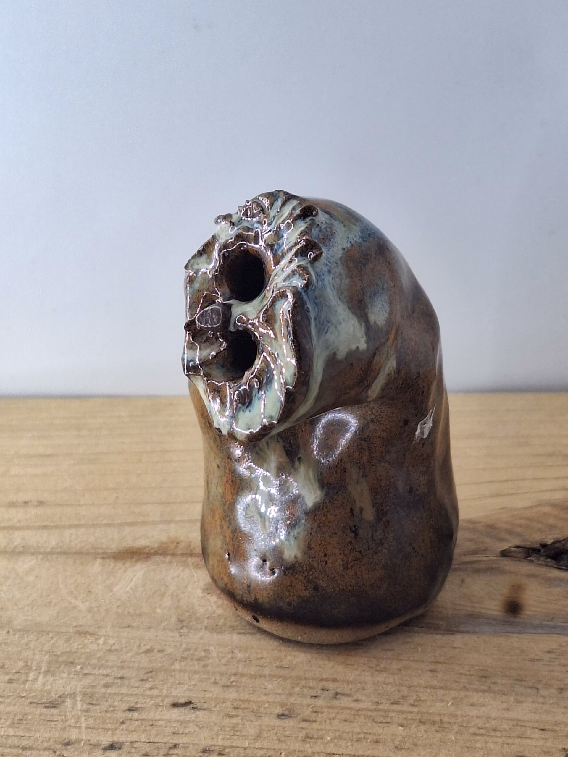 Small ceramic owl with a rounded body, textured surface in warm browns and creams, two dark hollow eyes, and a contemplative expression.
