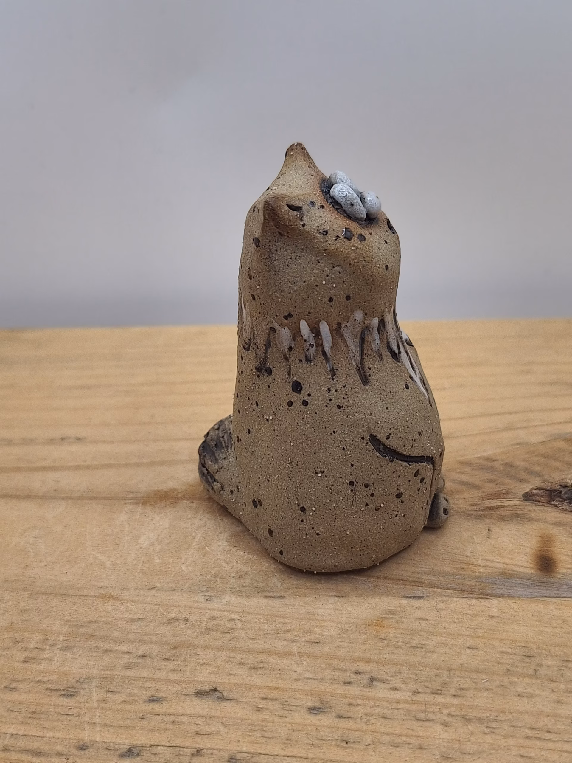 Small ceramic cat figurine with wide-set eyes, textured brown surface, and painted white markings on chest and face.