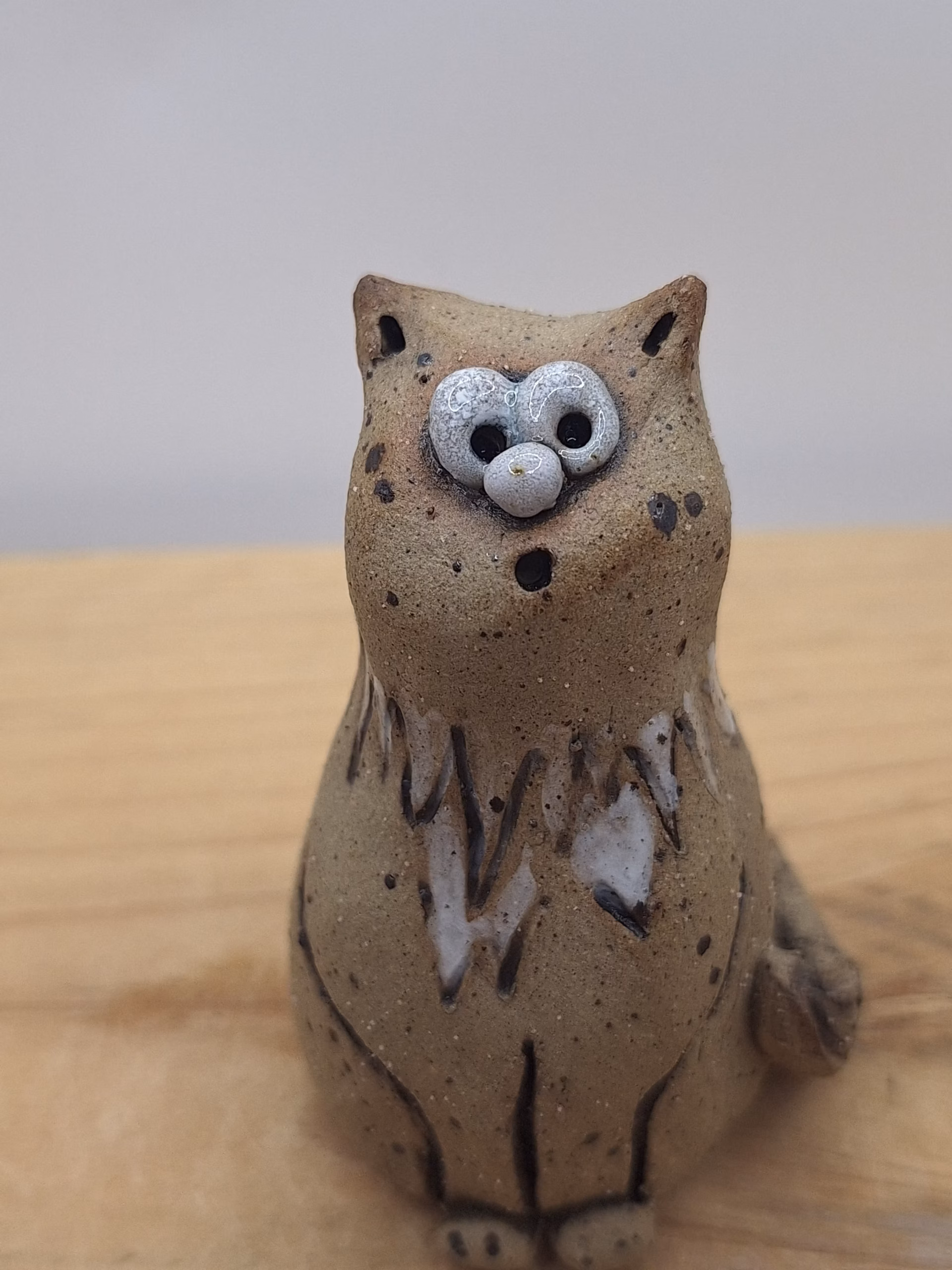 Small ceramic cat figurine with wide-set eyes, textured brown surface, and painted white markings on chest and face.