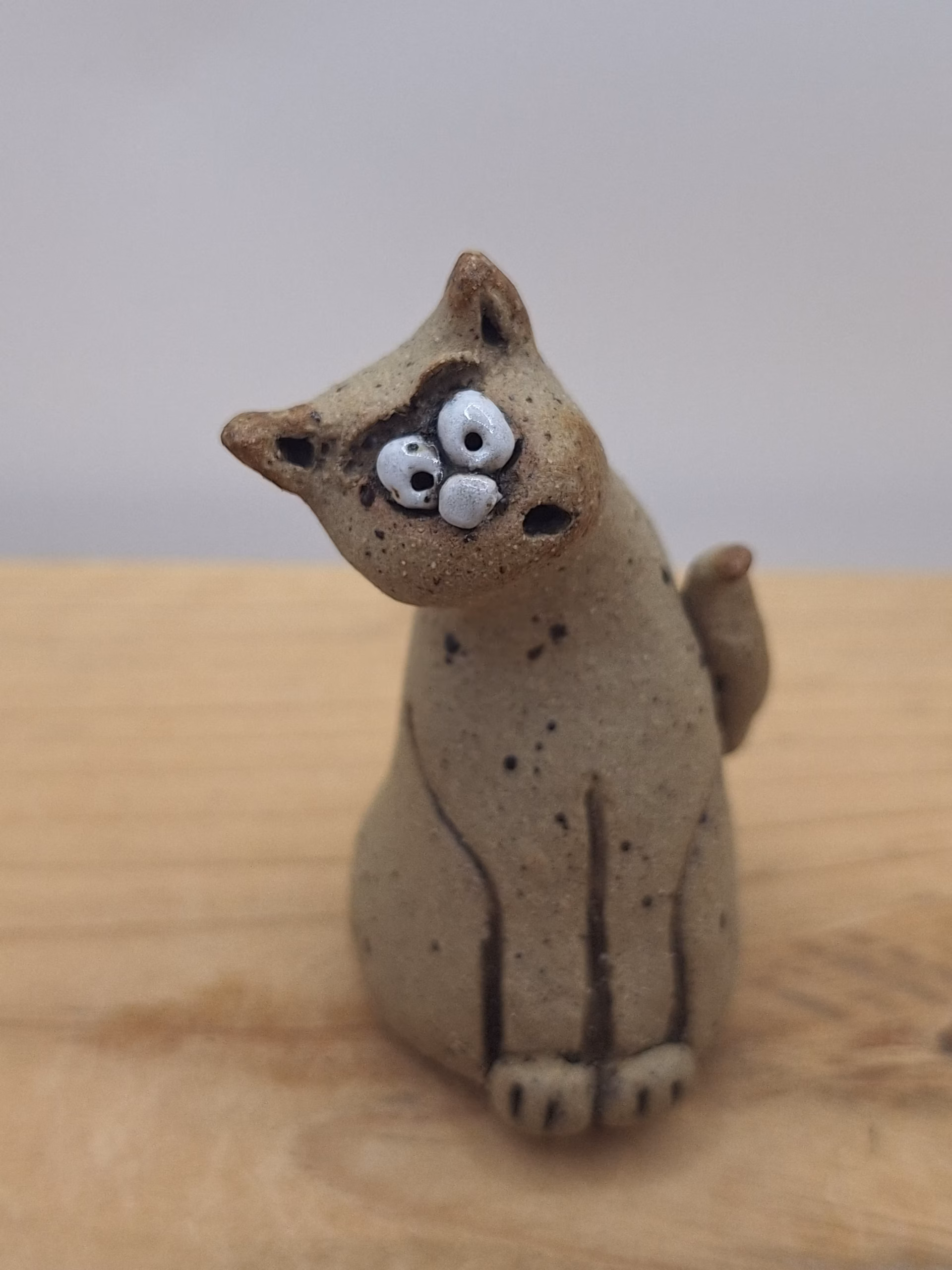 Small ceramic cat figurine with wide eyes and spotted surface, sitting upright with tail curved behind.