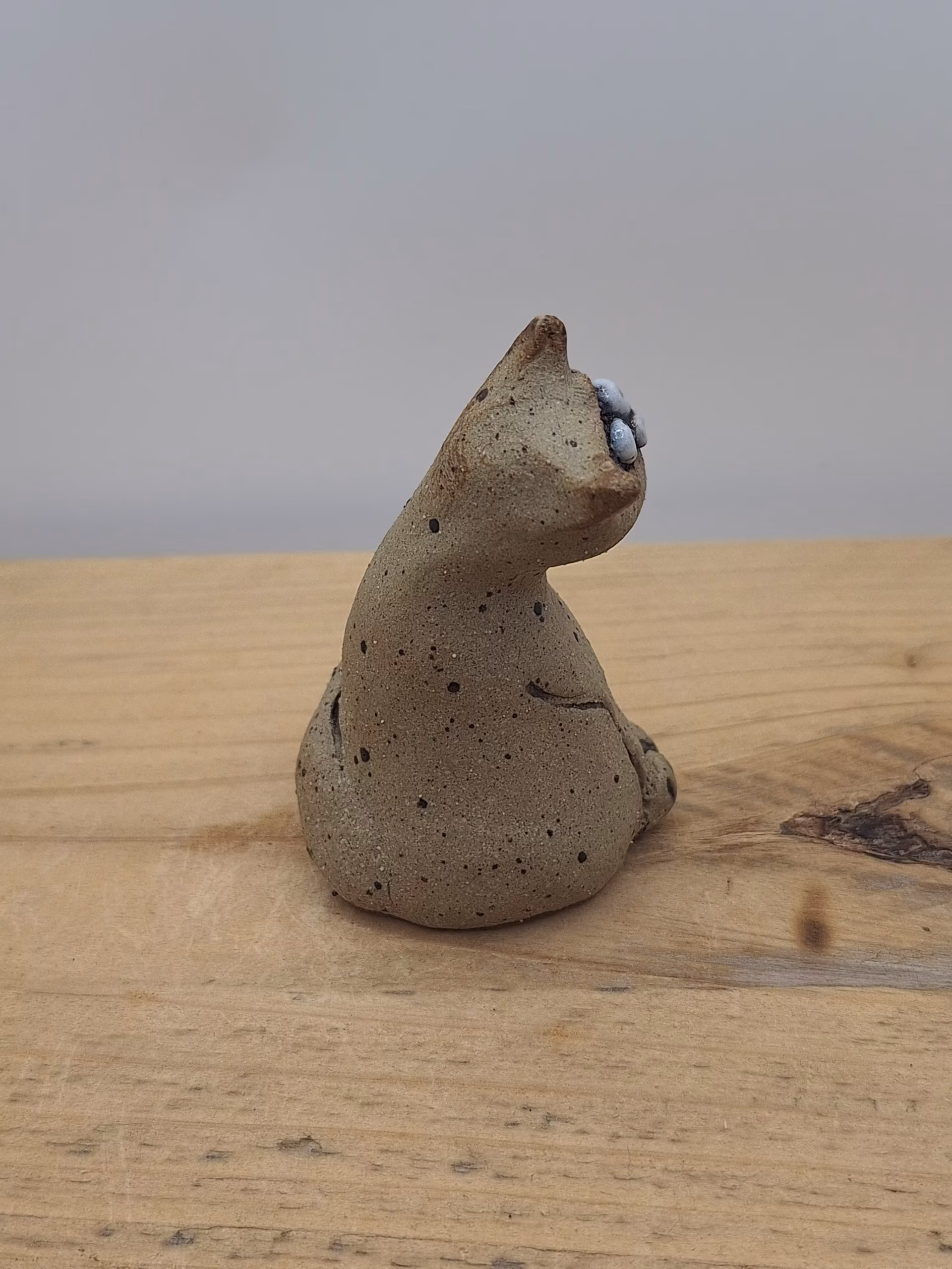 Small ceramic cat figurine with wide eyes and spotted surface, sitting upright with tail curved behind.