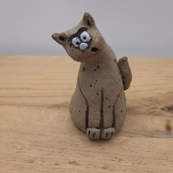 Small ceramic cat figurine with wide eyes and spotted surface, sitting upright with tail curved behind.