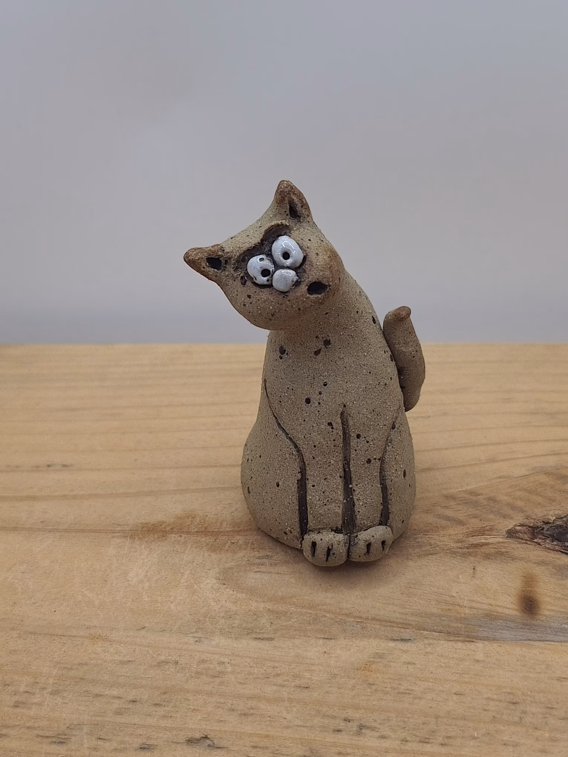 Small ceramic cat figurine with wide eyes and spotted surface, sitting upright with tail curved behind.