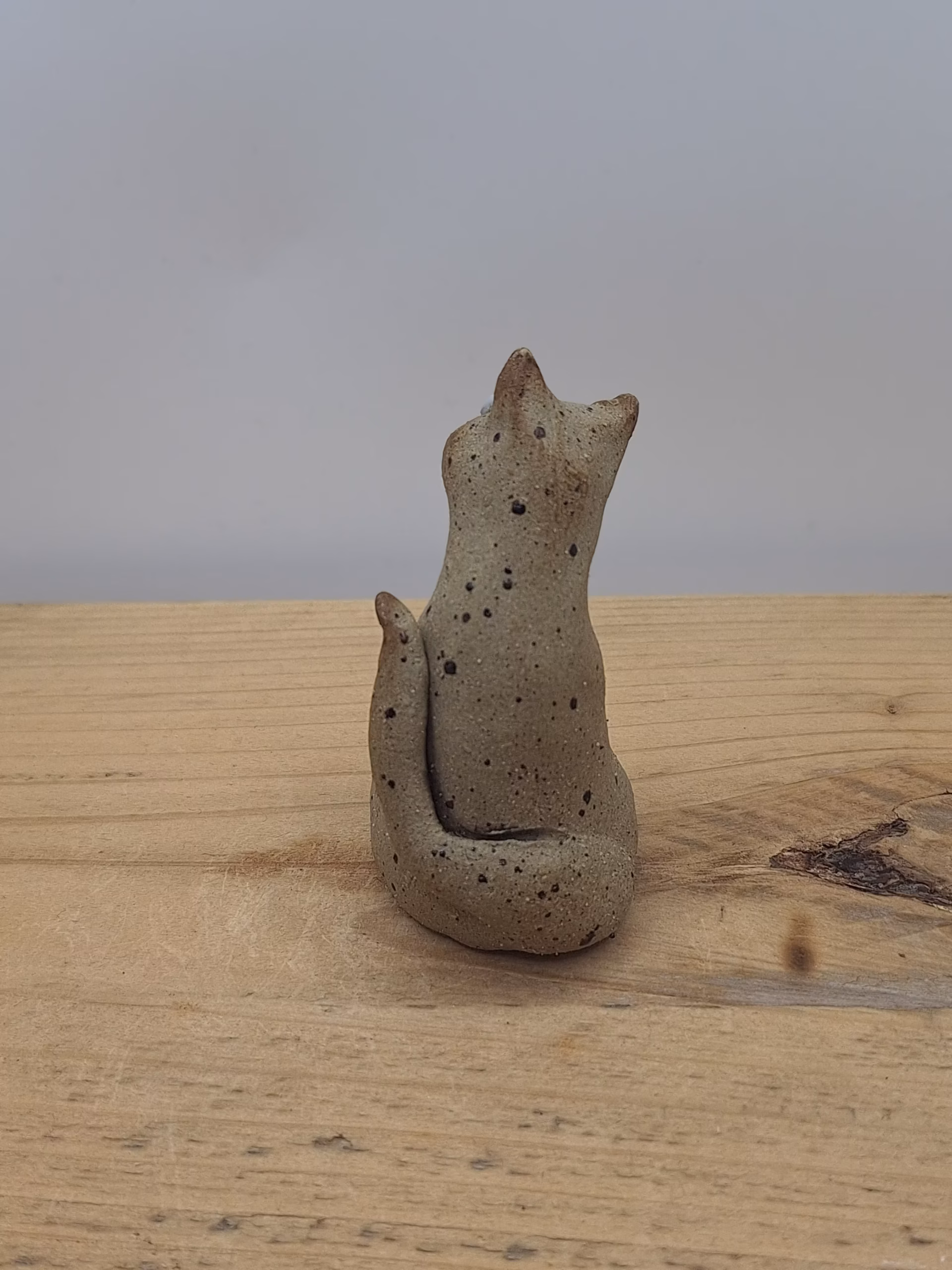 Small ceramic cat figurine with wide eyes and spotted surface, sitting upright with tail curved behind.