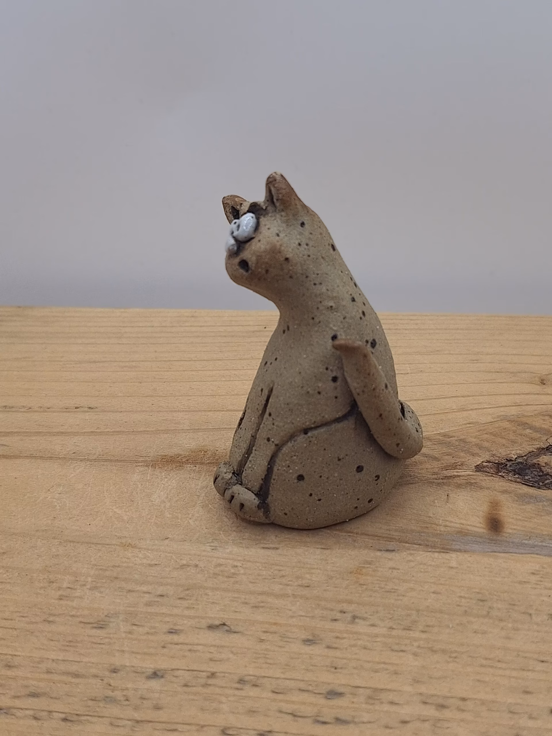 Small ceramic cat figurine with wide eyes and spotted surface, sitting upright with tail curved behind.