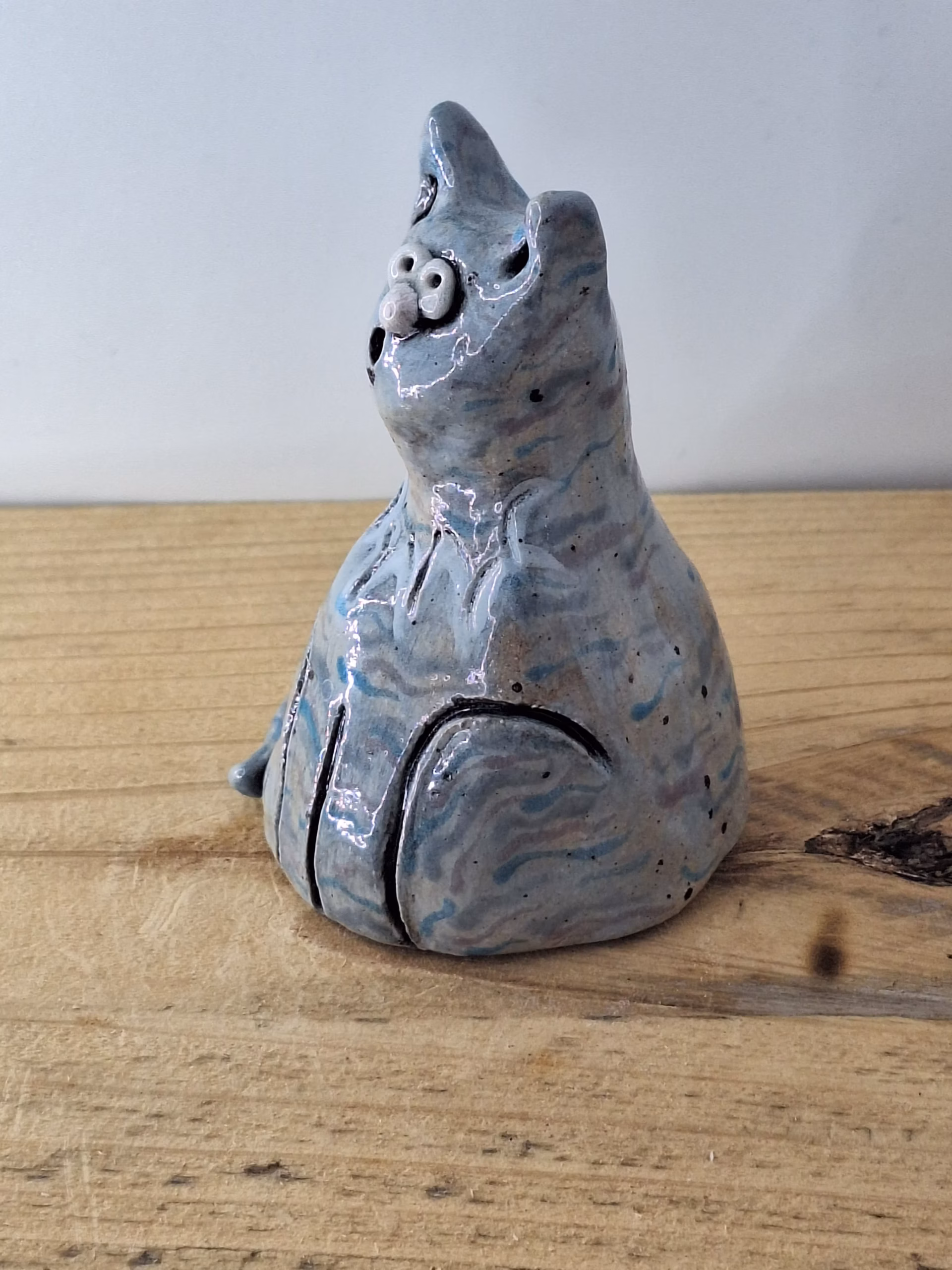 Small ceramic cat figurine with grey-blue glaze, white nose and eyes, black pupils and whiskers, seated upright.