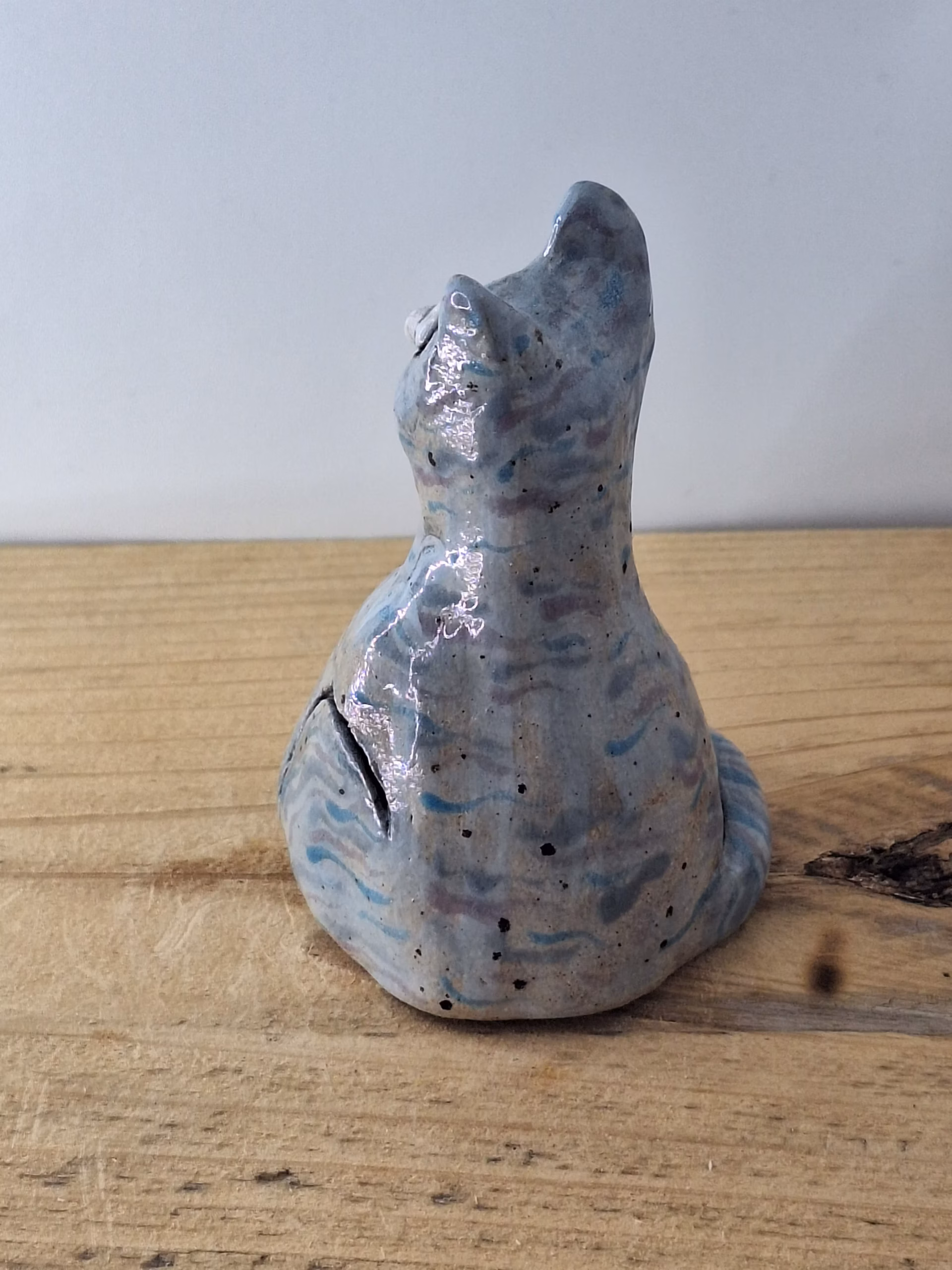 Small ceramic cat figurine with grey-blue glaze, white nose and eyes, black pupils and whiskers, seated upright.