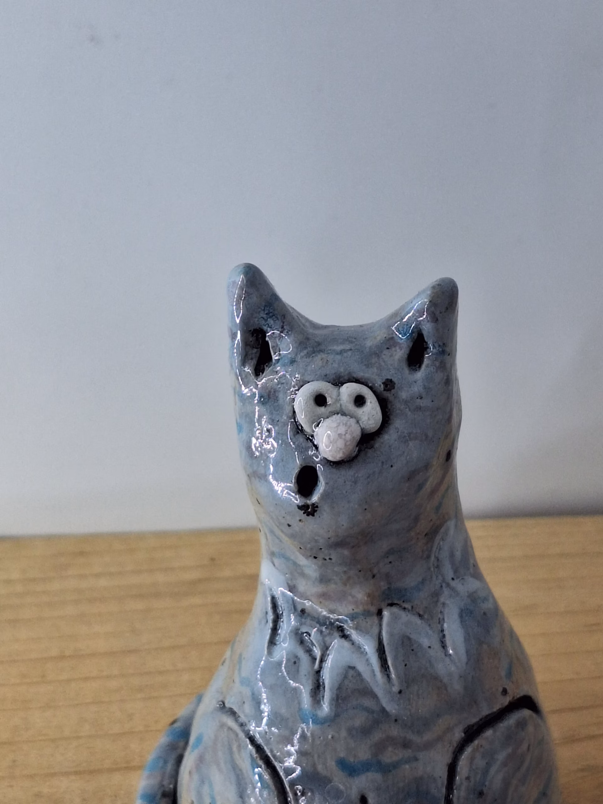 Small ceramic cat figurine with grey-blue glaze, white nose and eyes, black pupils and whiskers, seated upright.