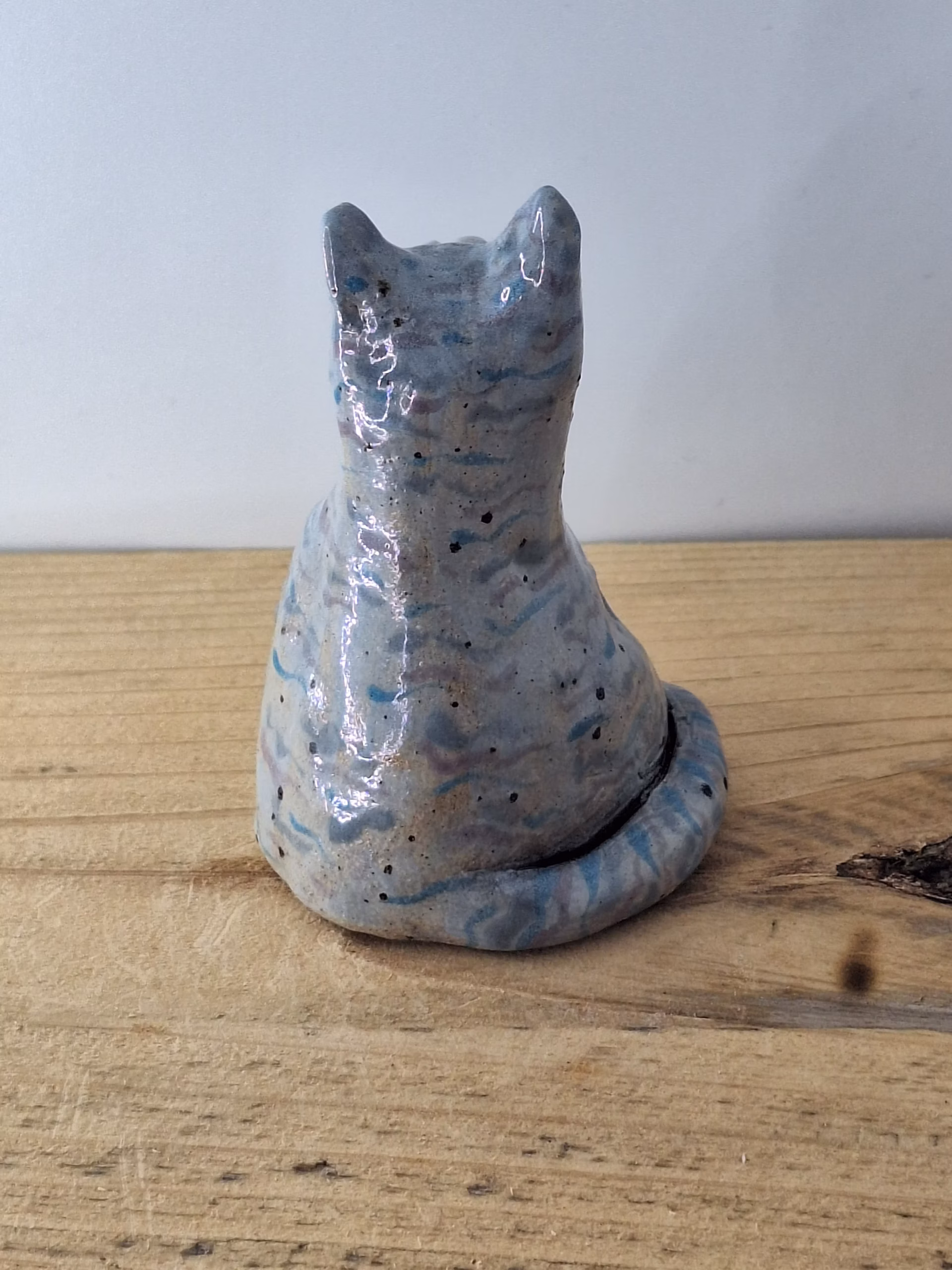 Small ceramic cat figurine with grey-blue glaze, white nose and eyes, black pupils and whiskers, seated upright.