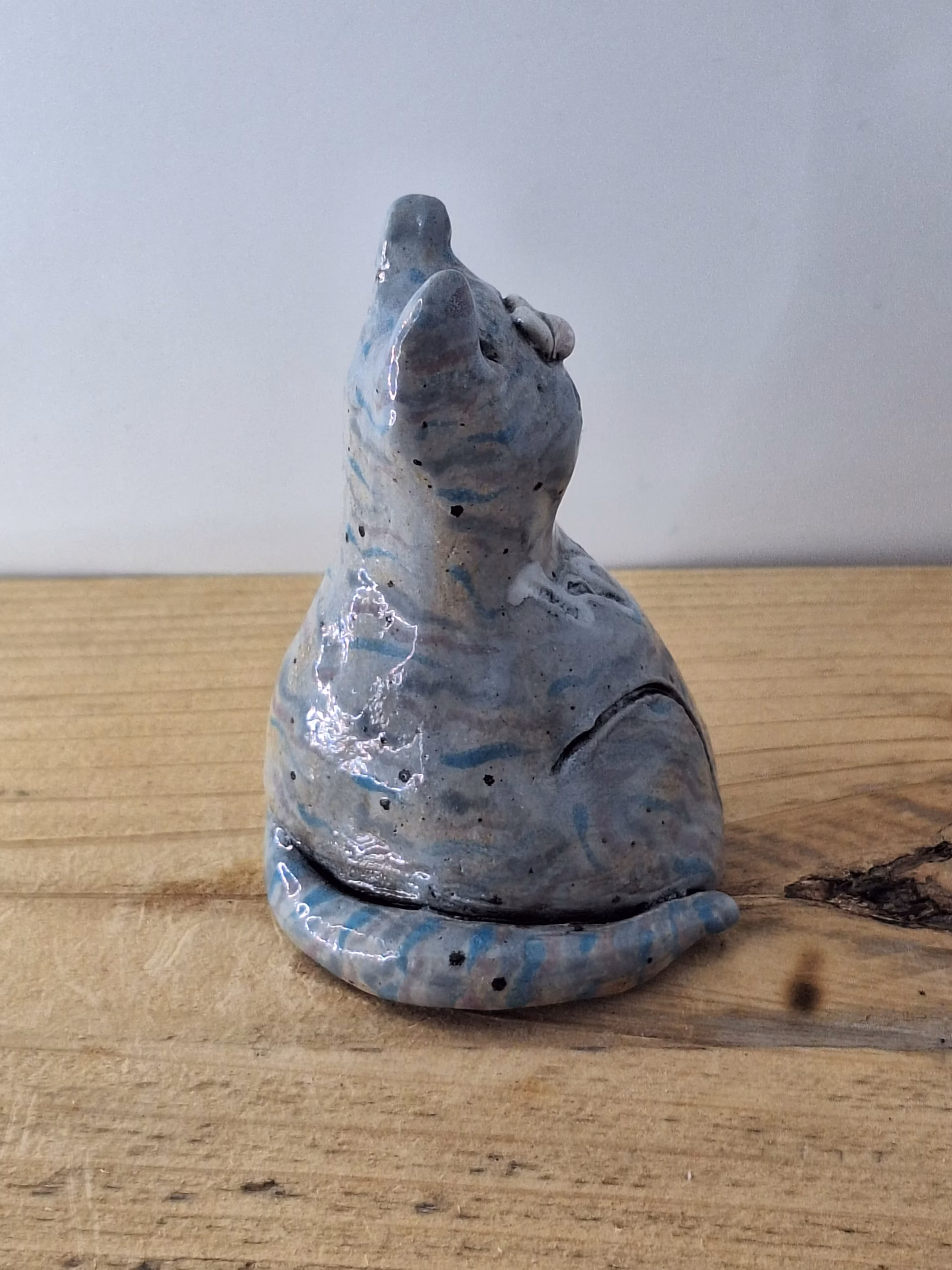 Small ceramic cat figurine with grey-blue glaze, white nose and eyes, black pupils and whiskers, seated upright.