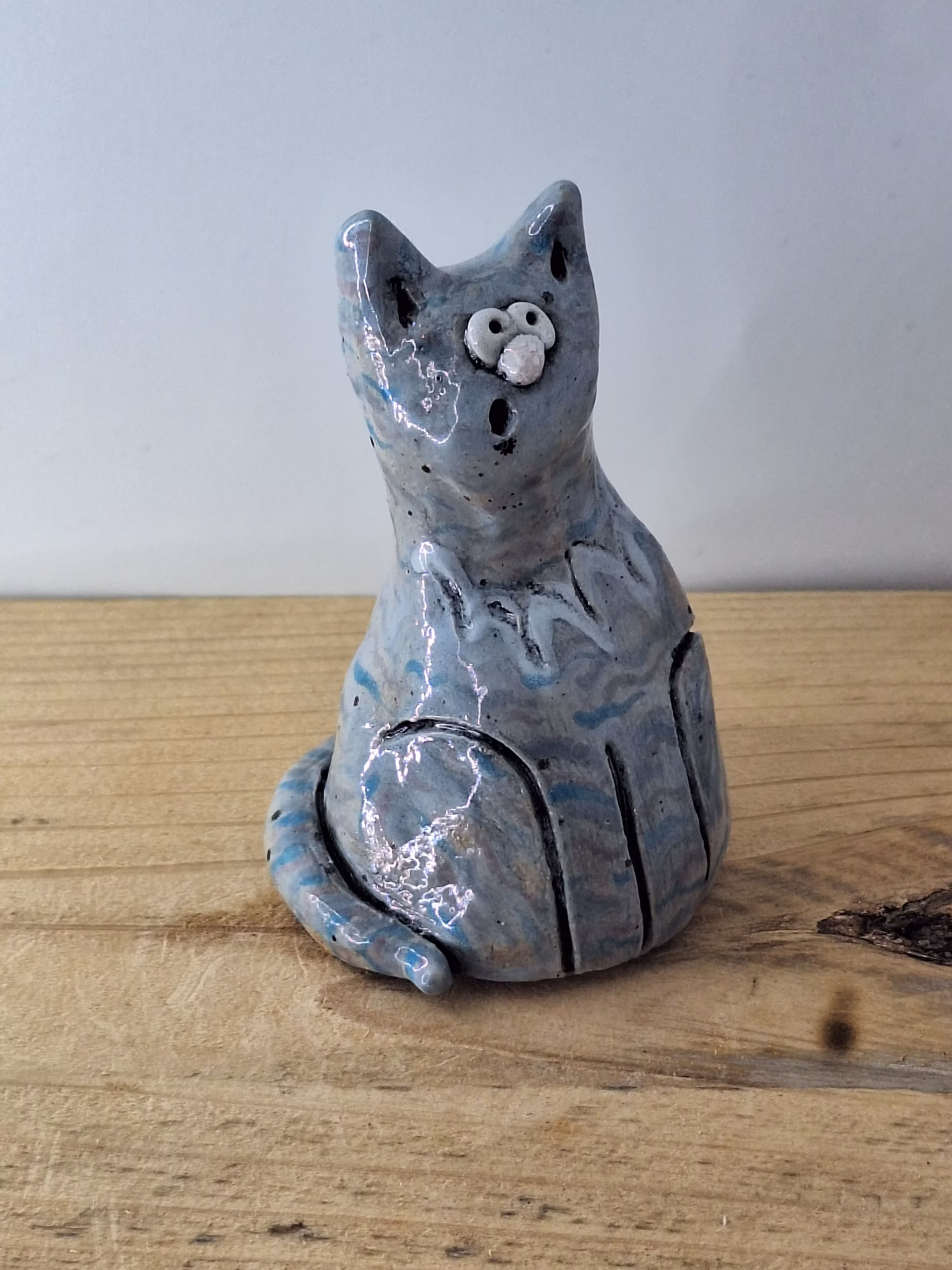 Small ceramic cat figurine with grey-blue glaze, white nose and eyes, black pupils and whiskers, seated upright.