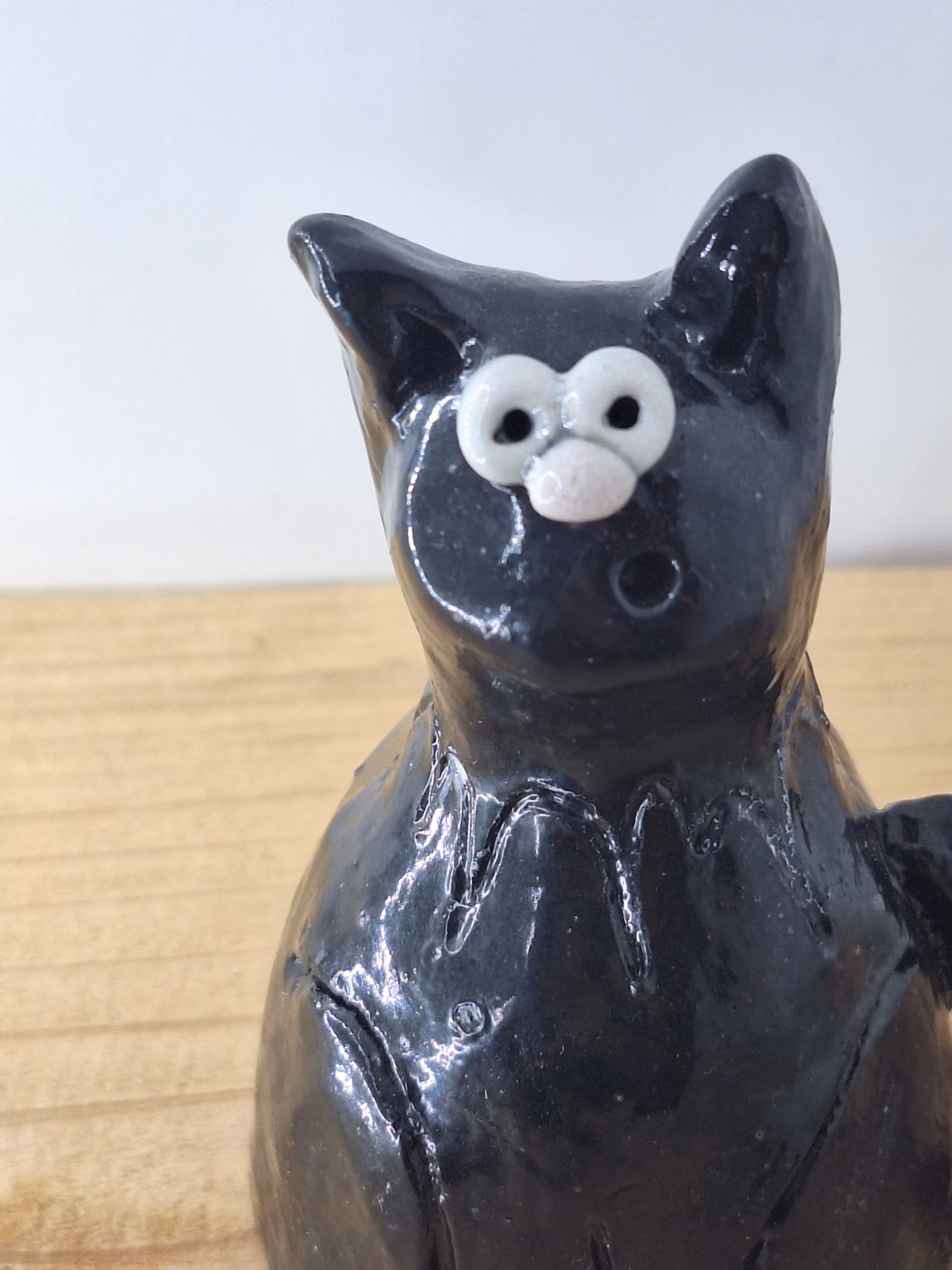 Small black ceramic cat with wide white eyes and pointed ears, sitting upright with a contemplative expression.