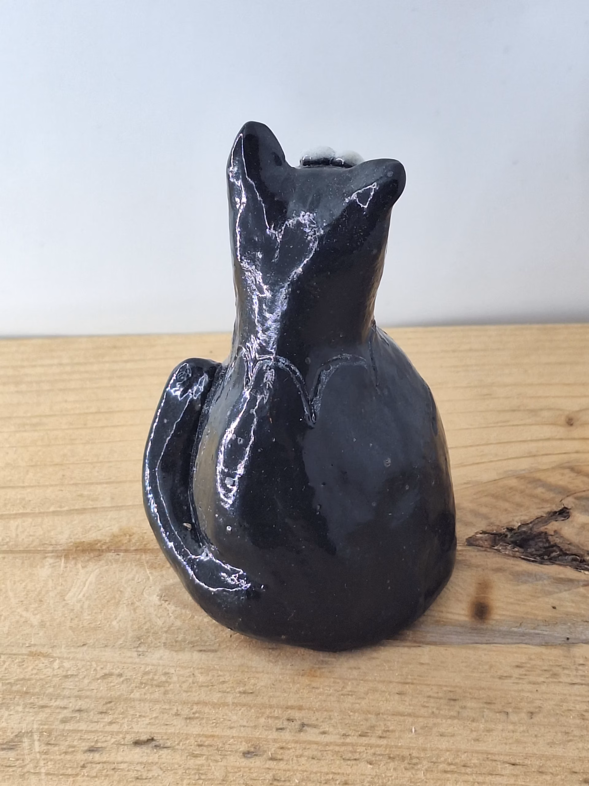 Small black ceramic cat with wide white eyes and pointed ears, sitting upright with a contemplative expression.