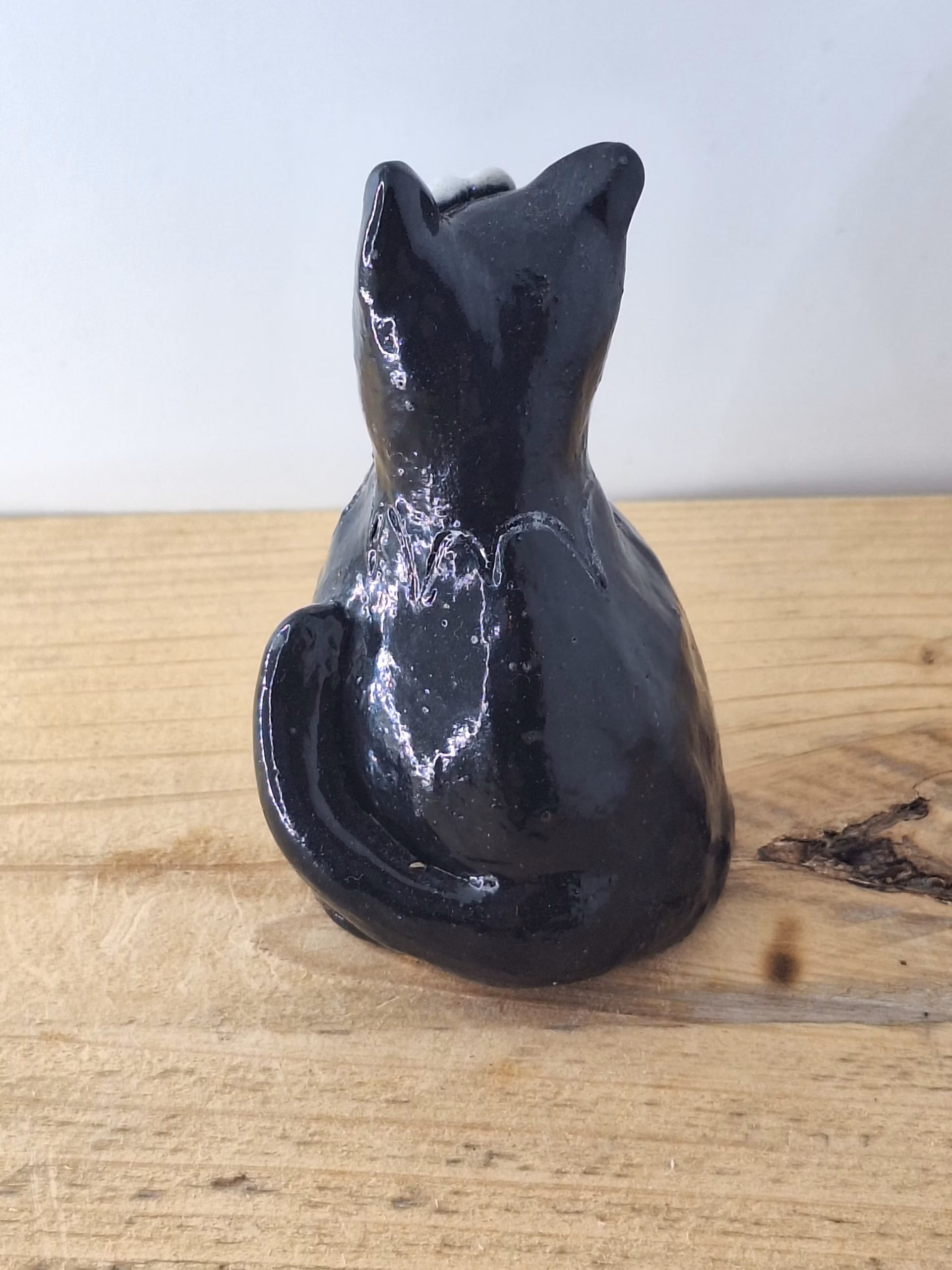 Small black ceramic cat with wide white eyes and pointed ears, sitting upright with a contemplative expression.